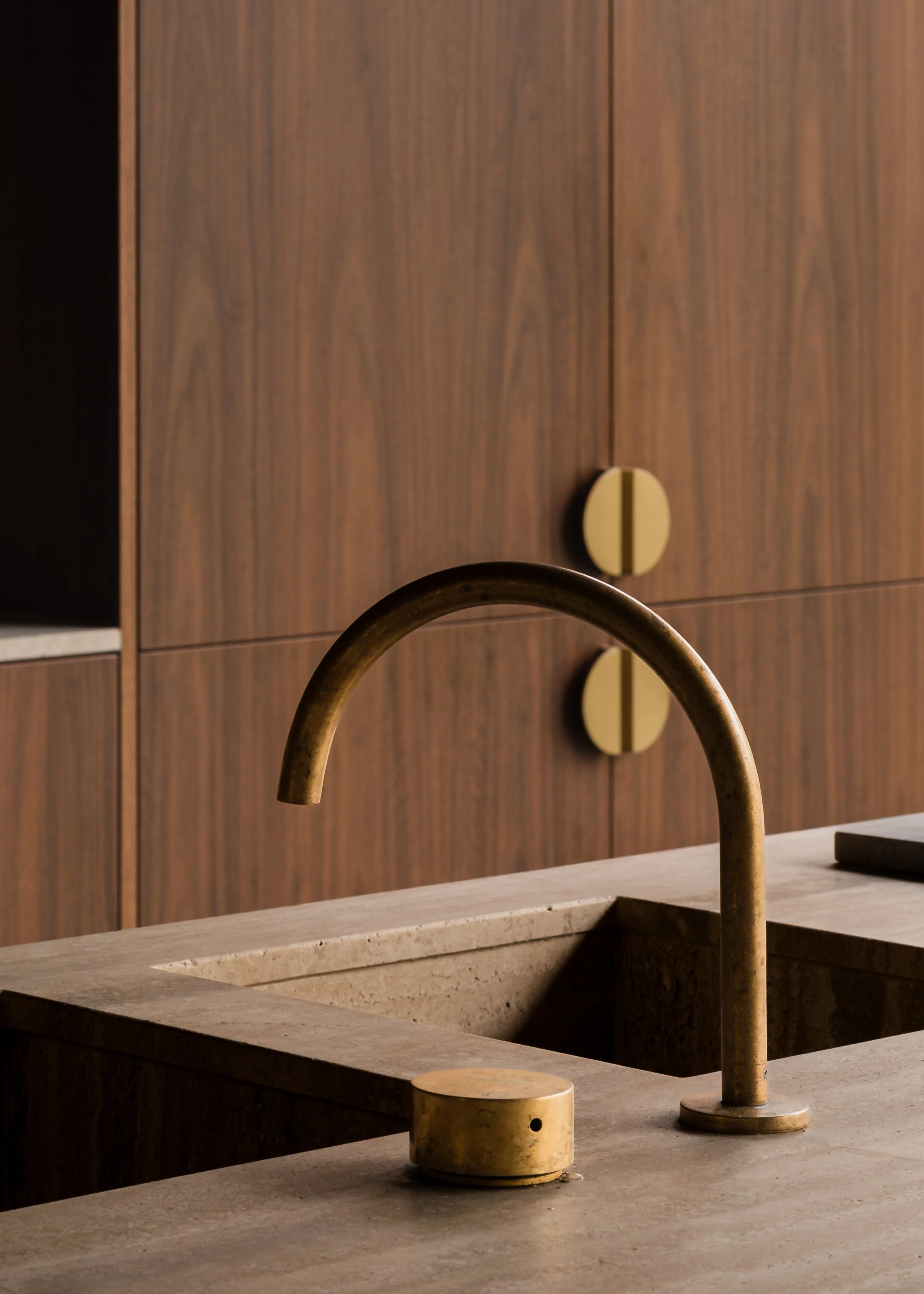 Brass kitchen tap and sink detail set against dark timber joinery and the travertine stone island at Matchbox.