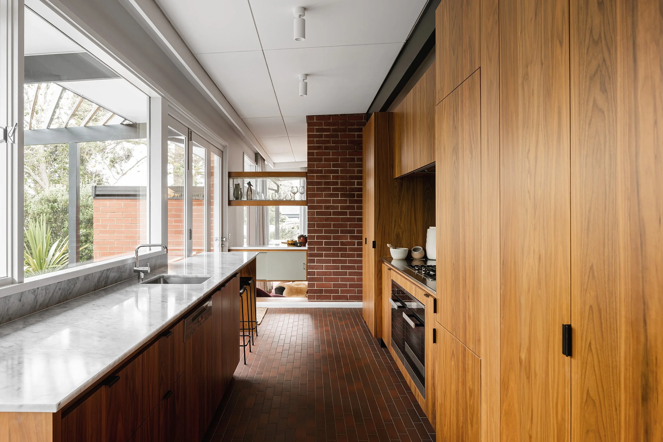 Mid century modern kitchen renovation by MRTN Architects, with walnut cabinetry, terracotta floor tiles and wide garden-facing windows.
