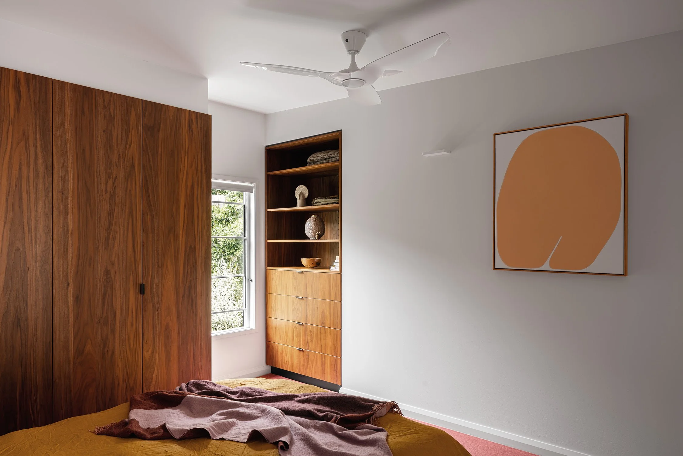 Mid century bedroom with walnut wardrobes, built-in shelves, mustard bedding and abstract artwork in Frankston, Australia.