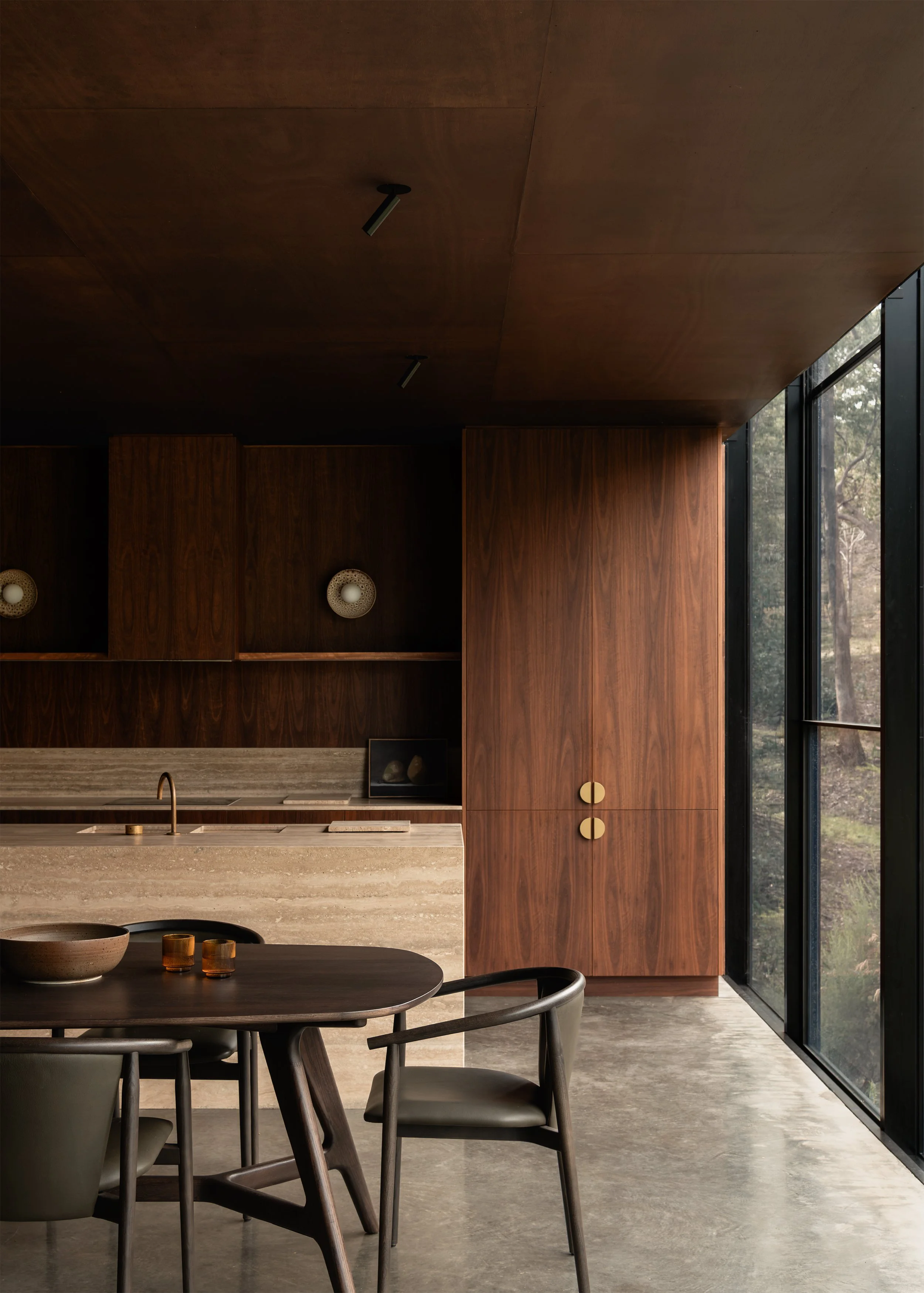 Dining area and dark timber kitchen beside full-height glazing to the bushland at Matchbox.
