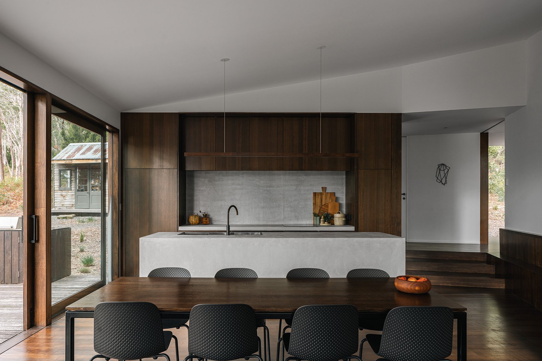 Dining and kitchen area at Killora Bay with a concrete island, dark timber cabinetry and large glazing to the outdoor deck.