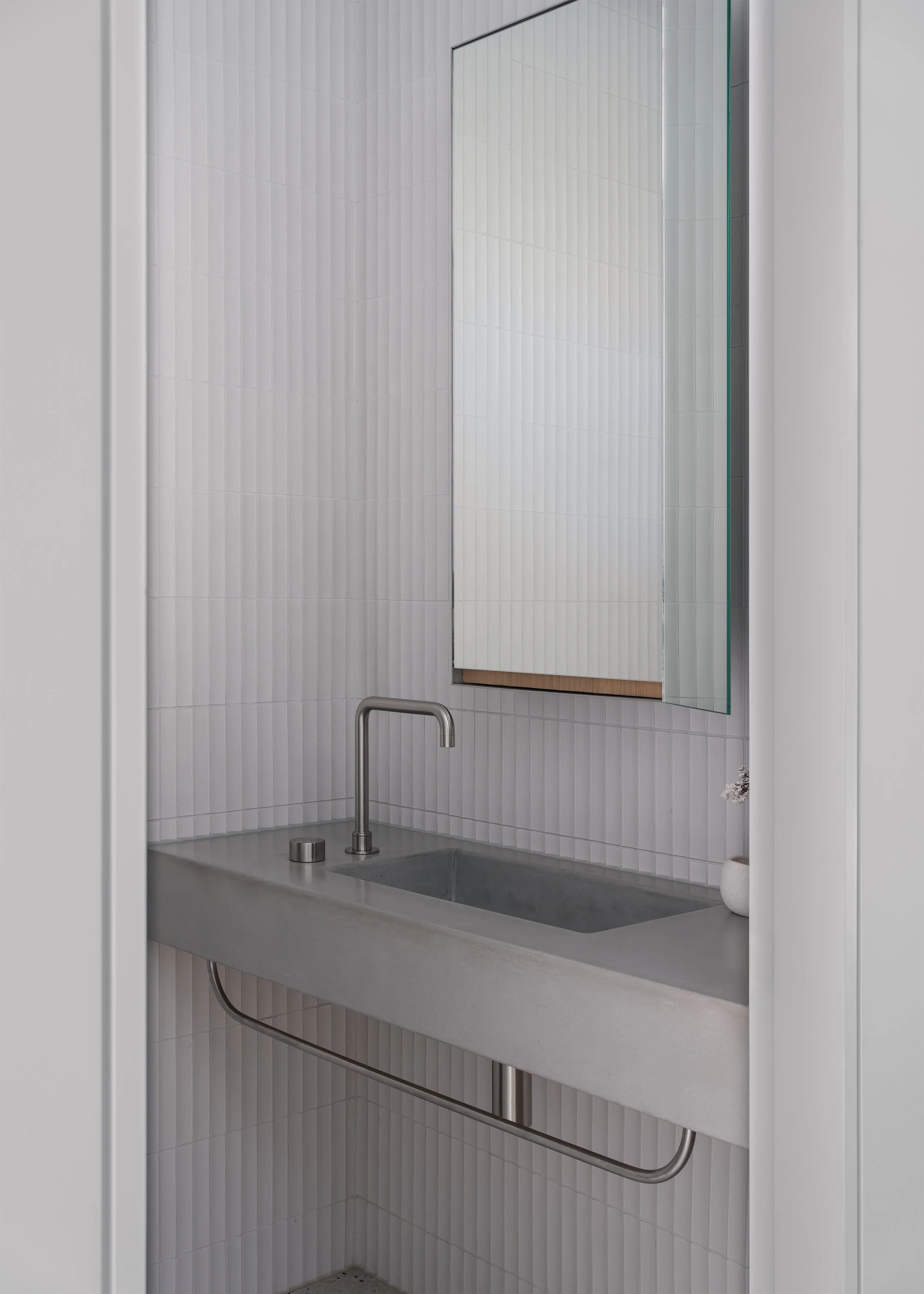 Minimal powder room with concrete basin, white vertical tiles and stainless steel fittings at Channel.