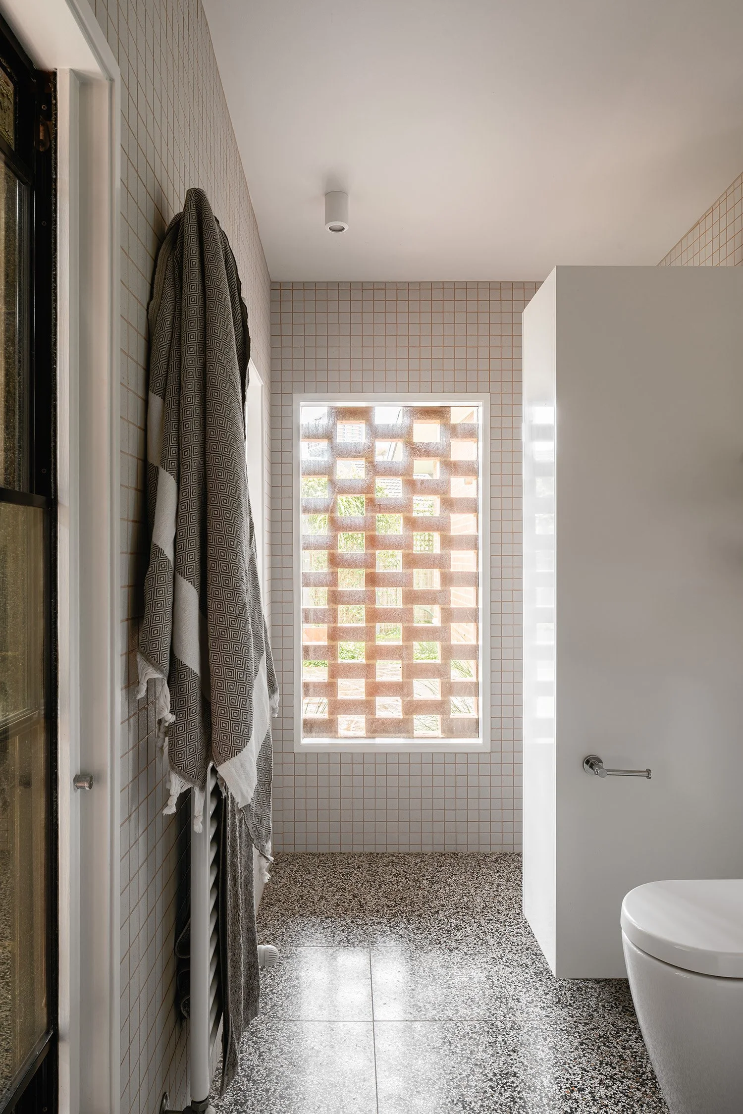 Contemporary bathroom in an Australian mid century home, with white square tiles, speckled flooring and a brick screen outside the window.