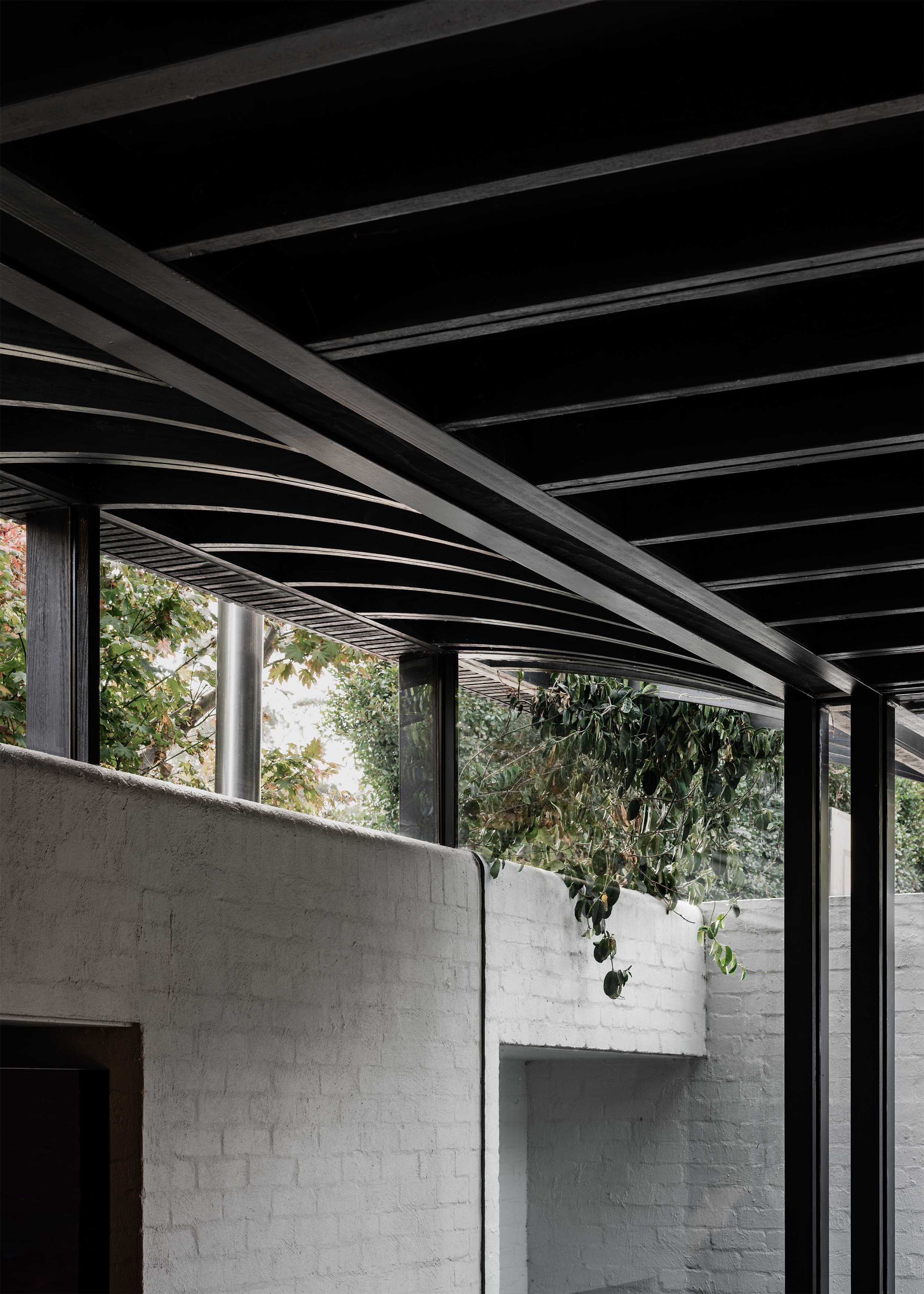 High masonry wall and clerestory glazing framing neighbouring trees beneath the dark timber roof.