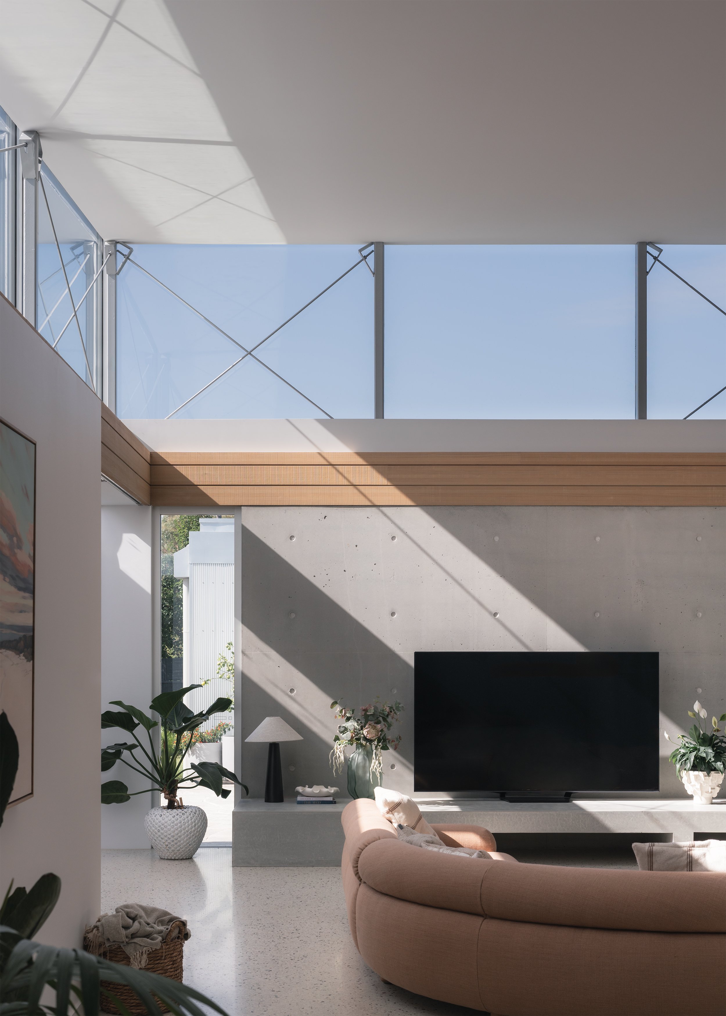 Living room with exposed concrete fireplace wall and dramatic sunlight entering through the clerestory glazing above.