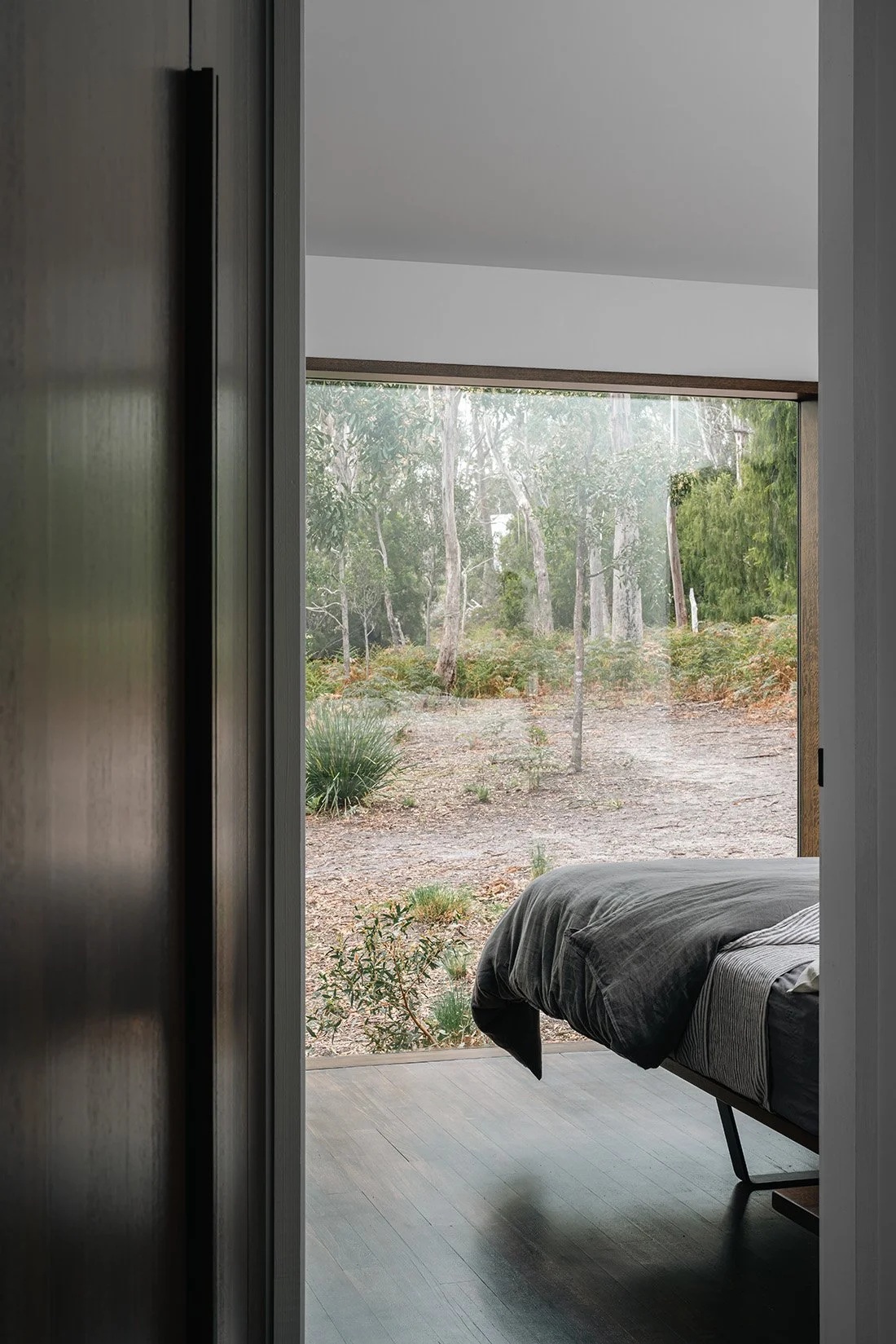Bedroom at Killora Bay viewed from the hallway, with full-height glazing overlooking the surrounding native bushland.
