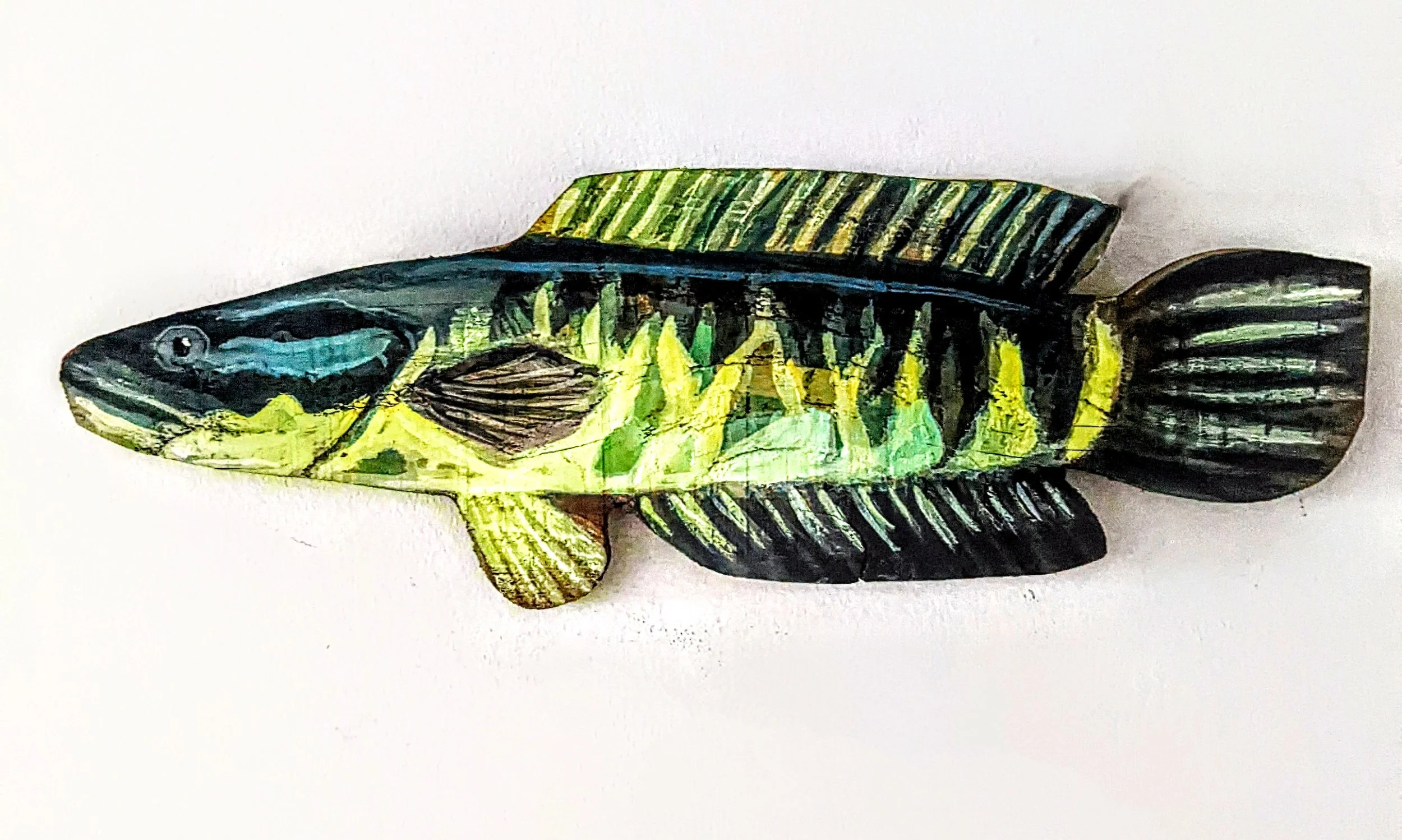 Painted fish cutout with black, yellow, green, and blue colors, featuring fin and scale details, placed on a white surface.