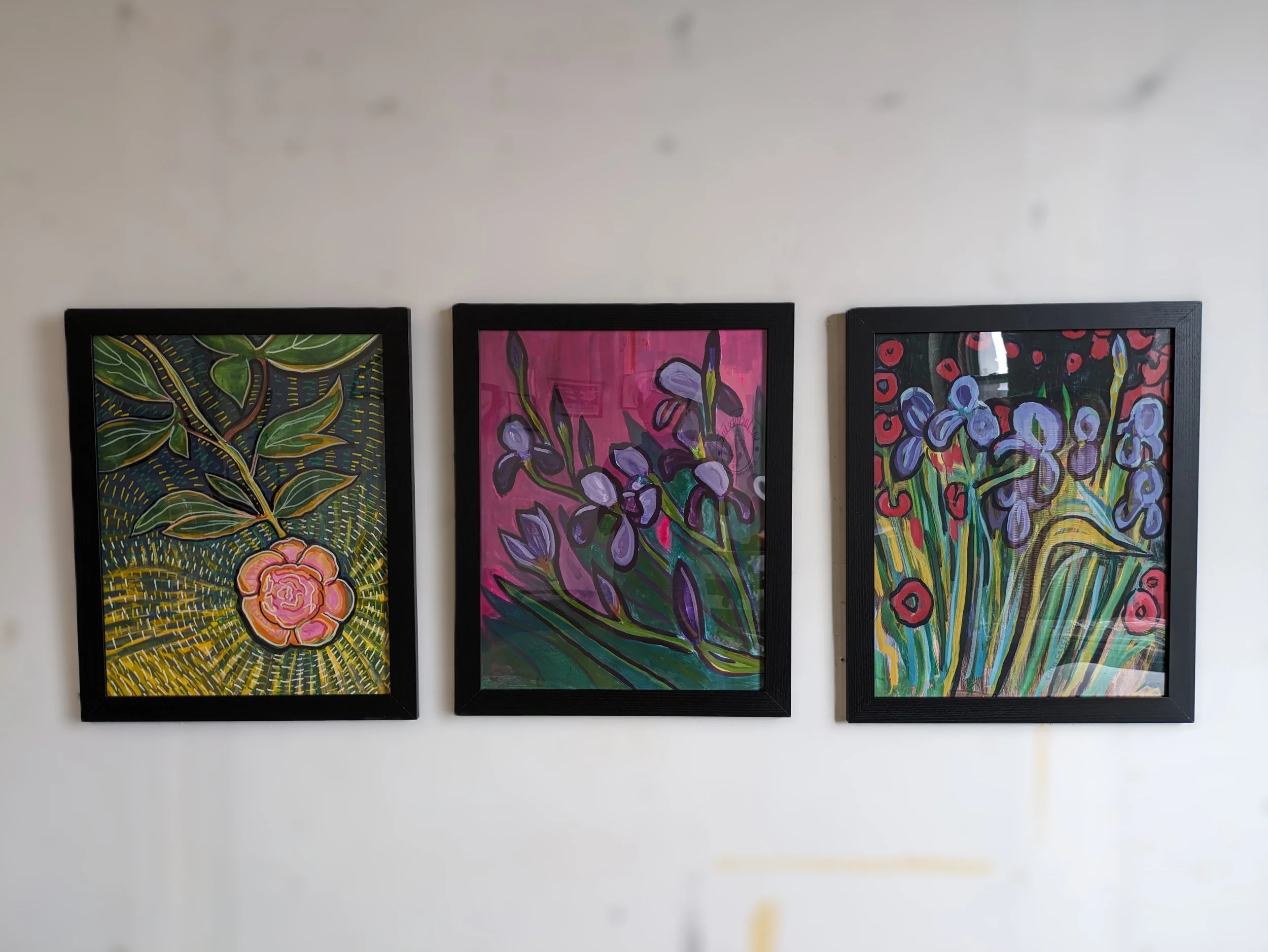 Three framed paintings of colorful flowers on a white wall.