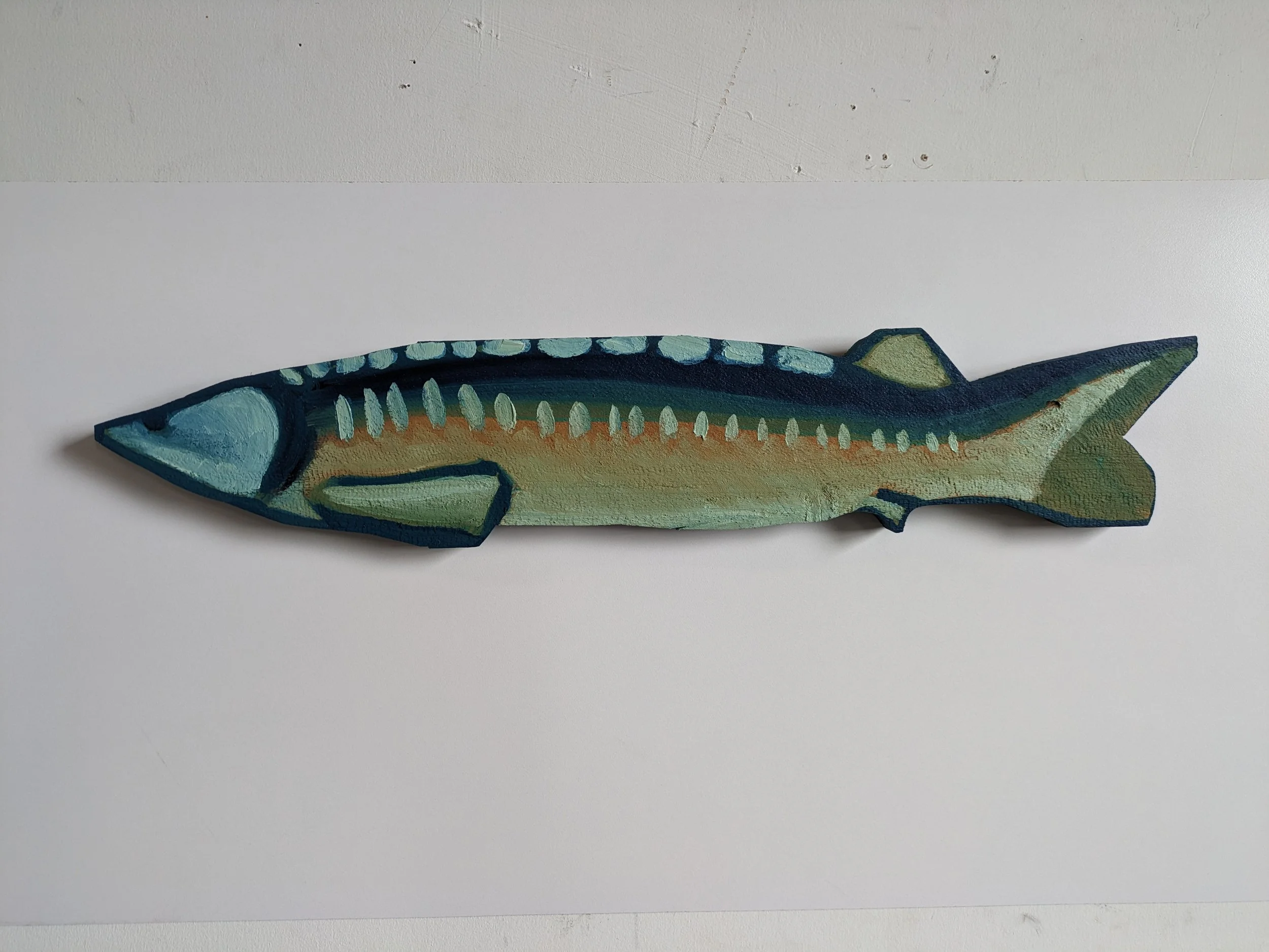 Painted wooden fish sculpture with blue, green, and beige colors on a white background.