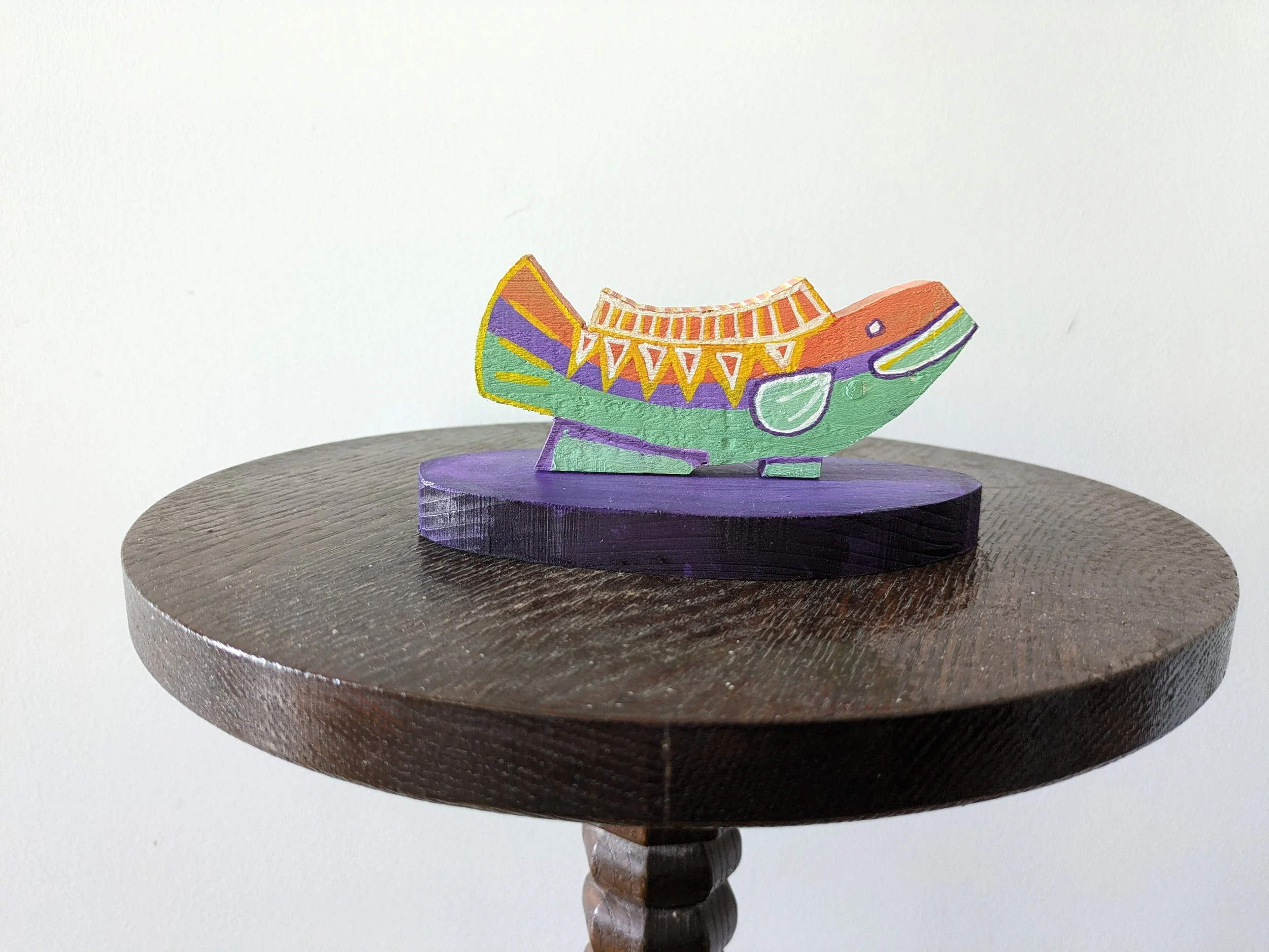 Colorful wooden fish sculpture with decorative patterns, placed on a dark wooden table.