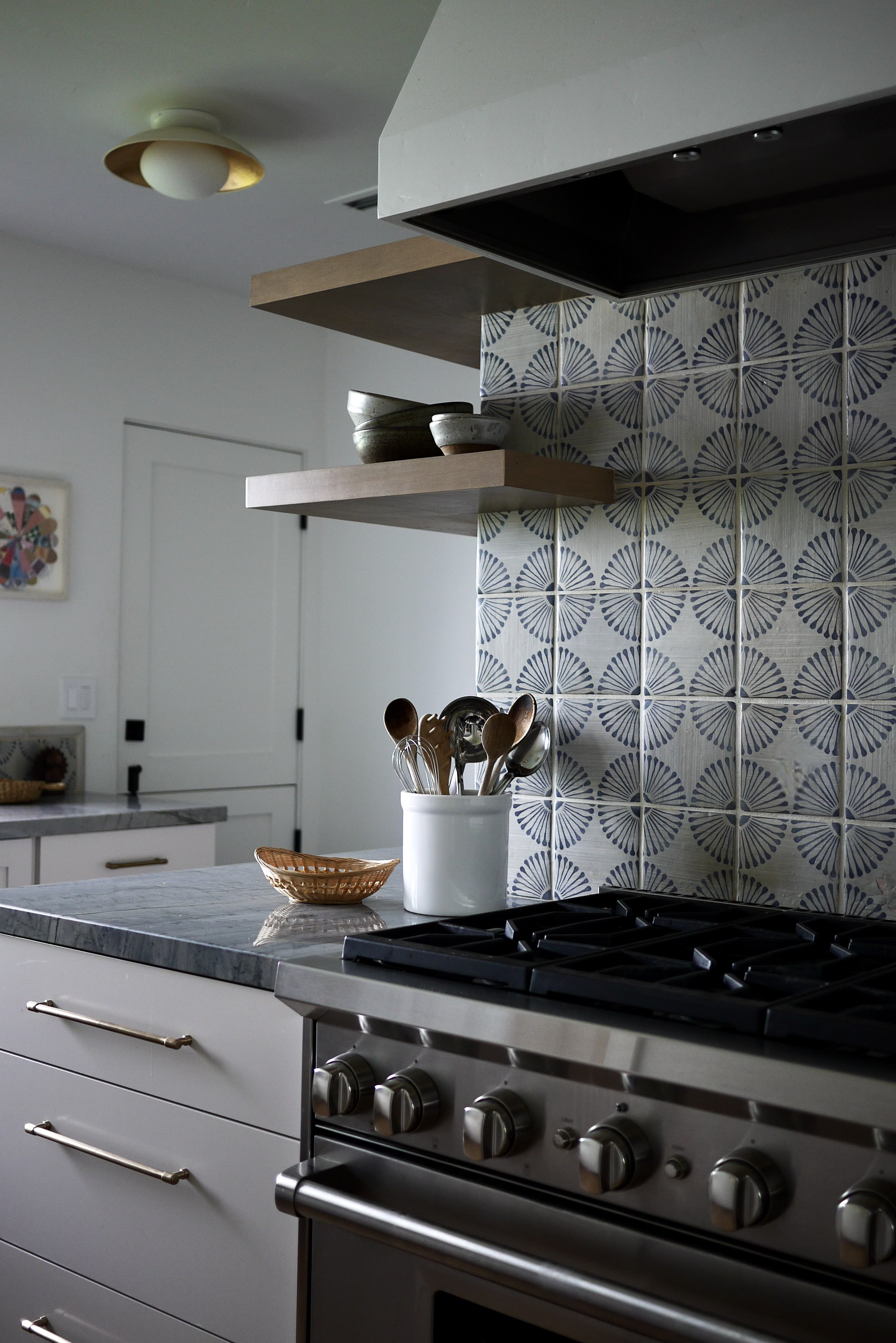 Modern kitchen with a gas stove, decorative tile backsplash, floating shelves with bowls, and countertop utensils in a holder.