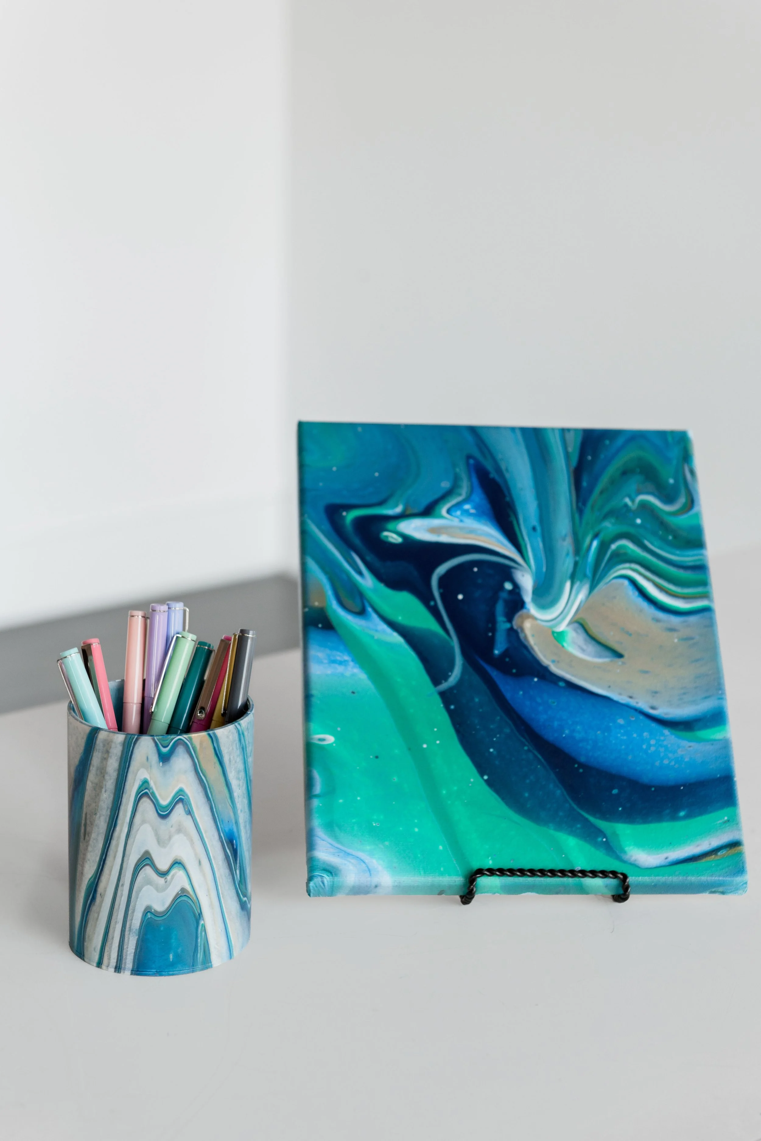 Pour painted desk organizer with pens beside a matching acrylic pour painted canvas, a custom corporate gift