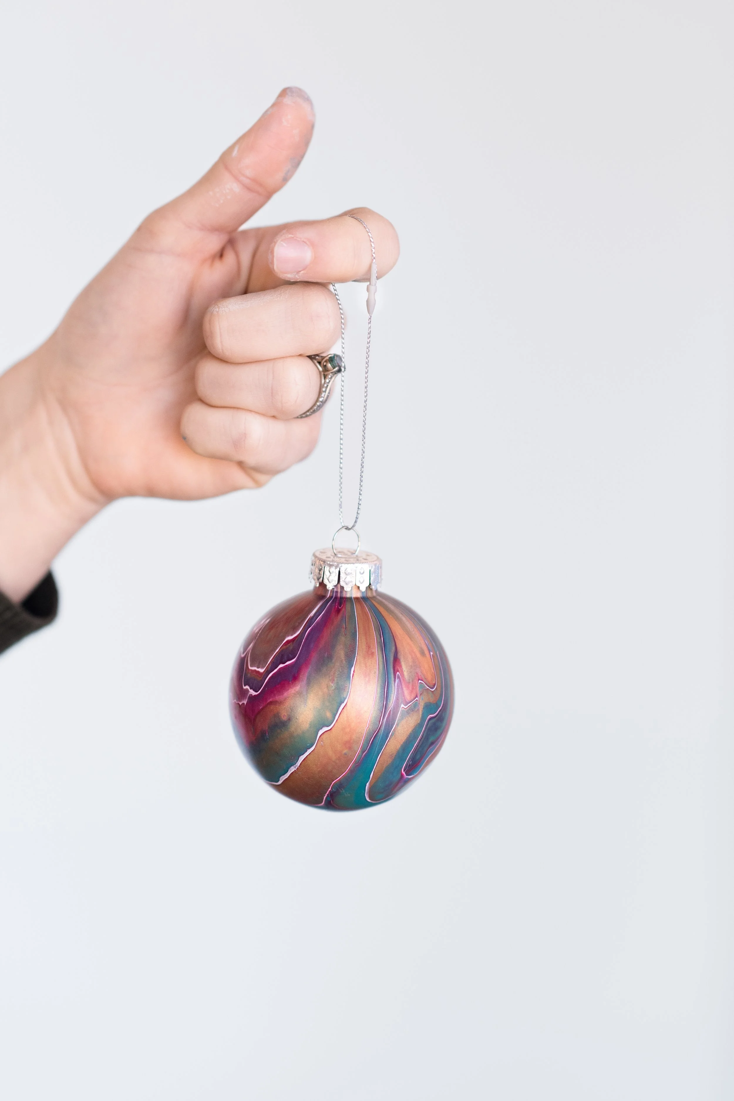 Hand holding an acrylic pour painted Christmas ornament from a corporate holiday gift kit