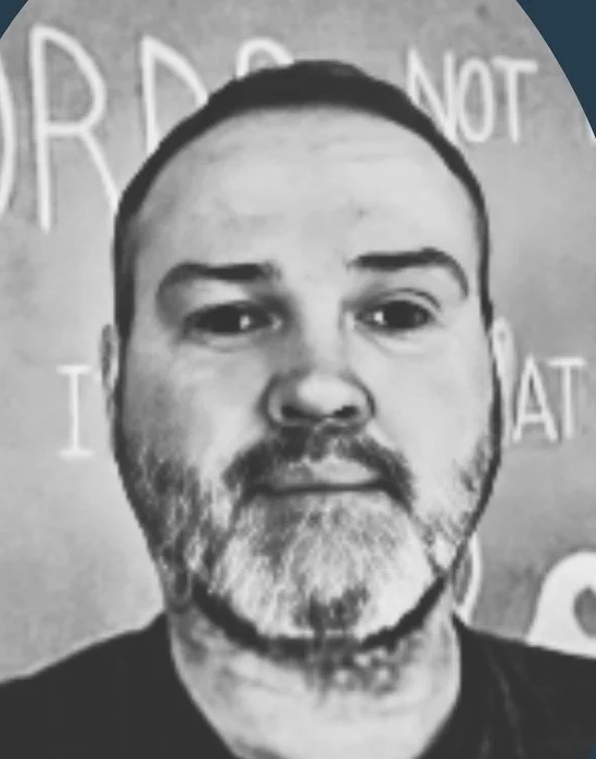 Man with facial hair in front of a wall with motivational text.