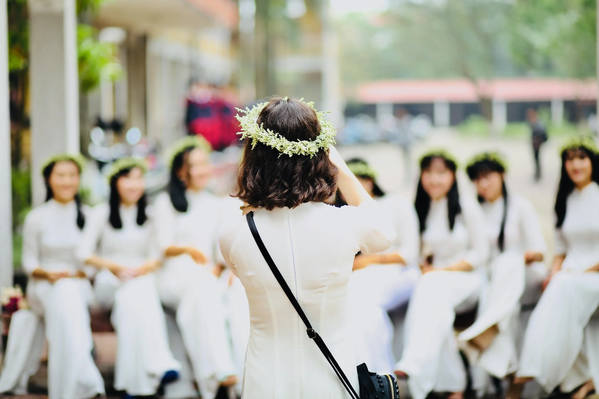 Group of women in white dresses and floral crowns posing for a photo taken by another woman