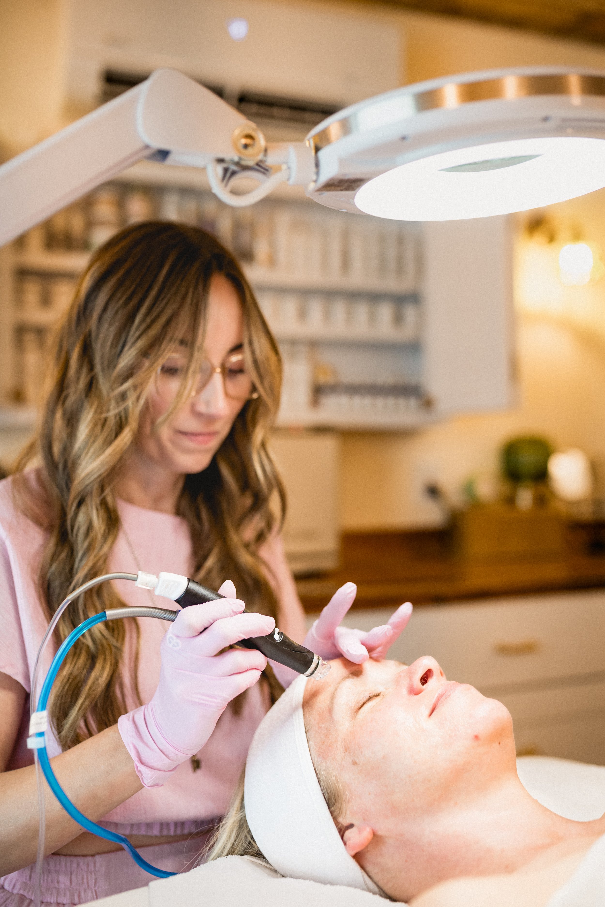 A beautician performing a laser skin treatment on a woman lying down with eyes closed, in a spa or clinic setting.