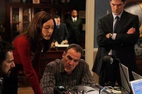 Lola Glaudini as Elle Greenaway in "Criminal Minds" seen looking over Mandy Patinkin's shoulder in a serious discussion at a desk in the police station.