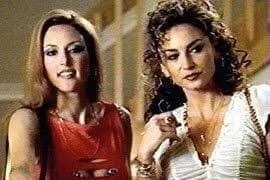 Lola Glaudini in the "Sopranos." Two women standing close together, one with long straight hair wearing a red dress, the other with curly hair wearing a white top and necklace.