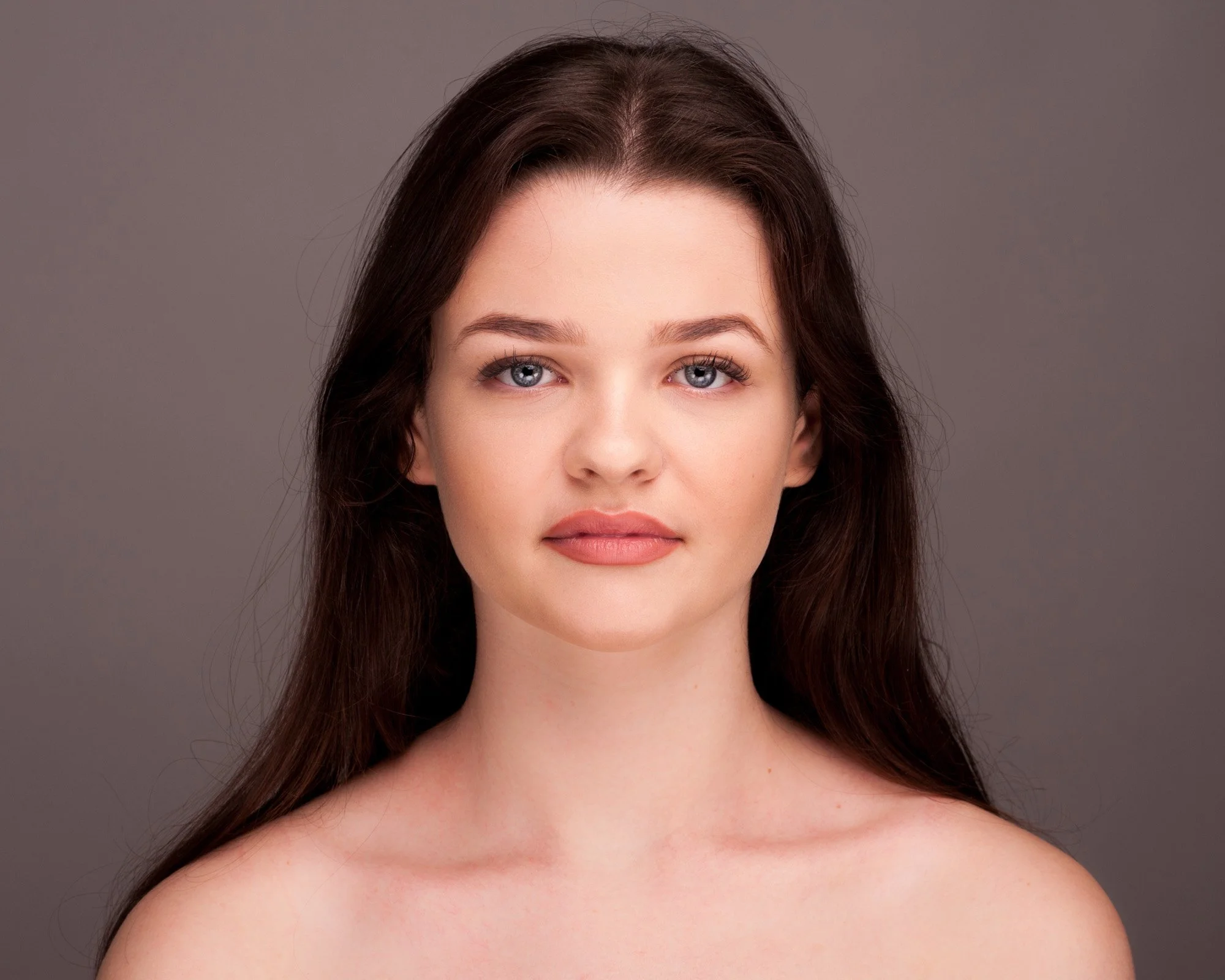 A young woman with fair skin, blue eyes, and long brown hair against a plain gray background.
