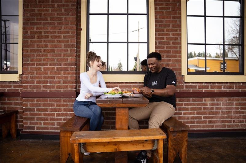 Two people sitting at a bench table outside by a brick wall on a patio enjoying a meal