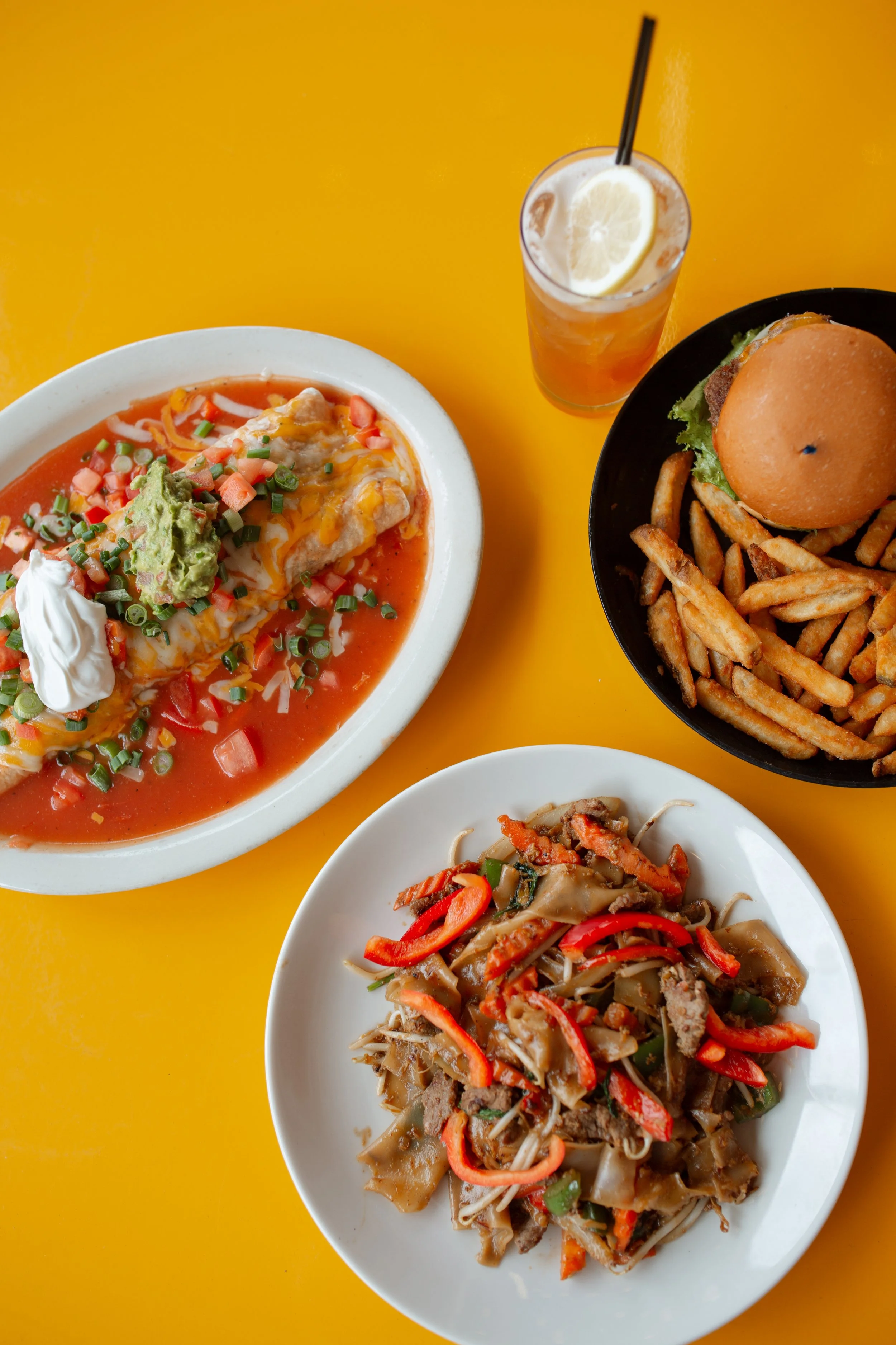Image of a burger and fries, a thai noodle dish with red peppers, and a Mexican burrito with salsa, cheese, sour cream, and guacamole