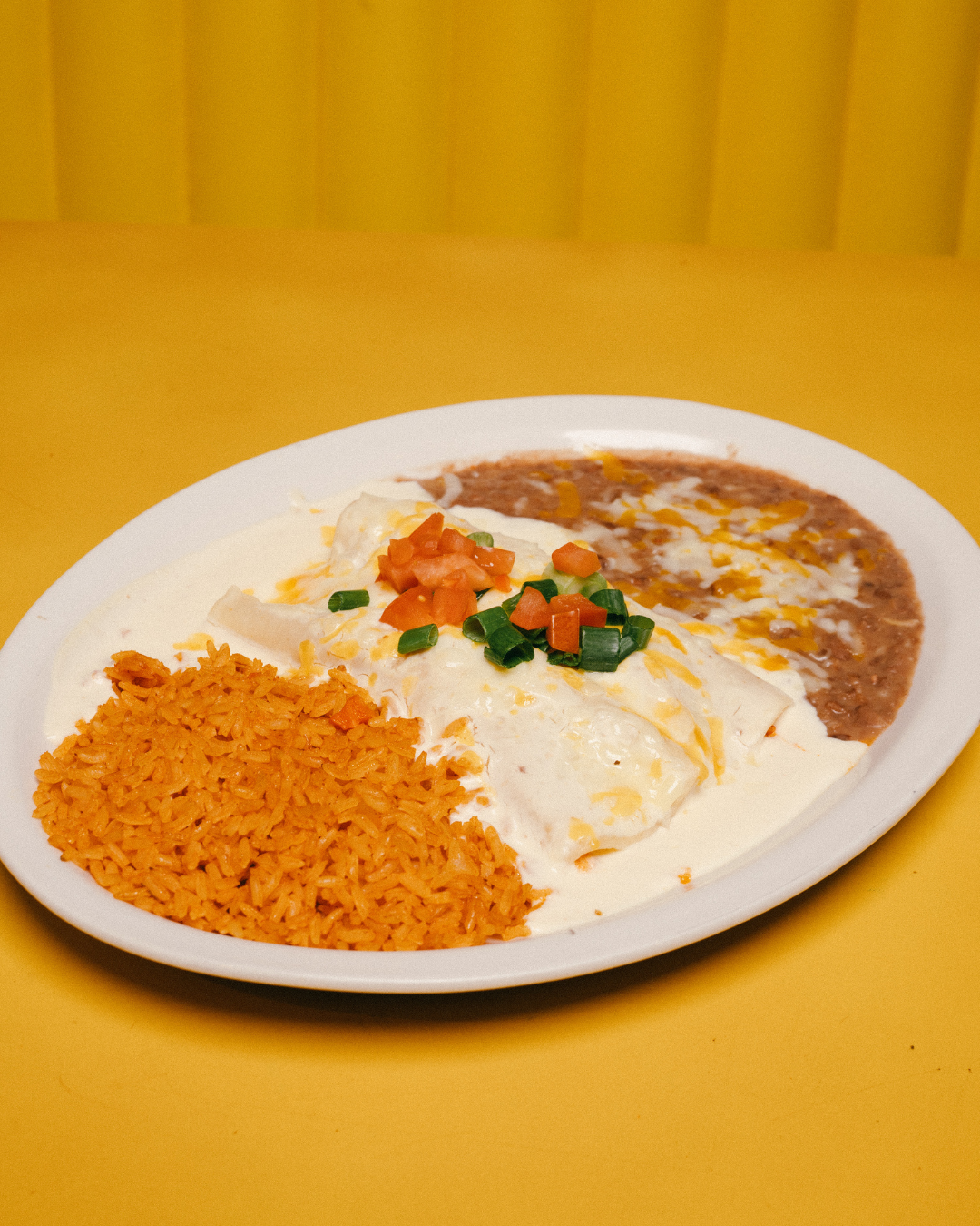 Plate with Mexican food including rice, beans, and a creamy dish topped with chopped green onions and tomatoes.