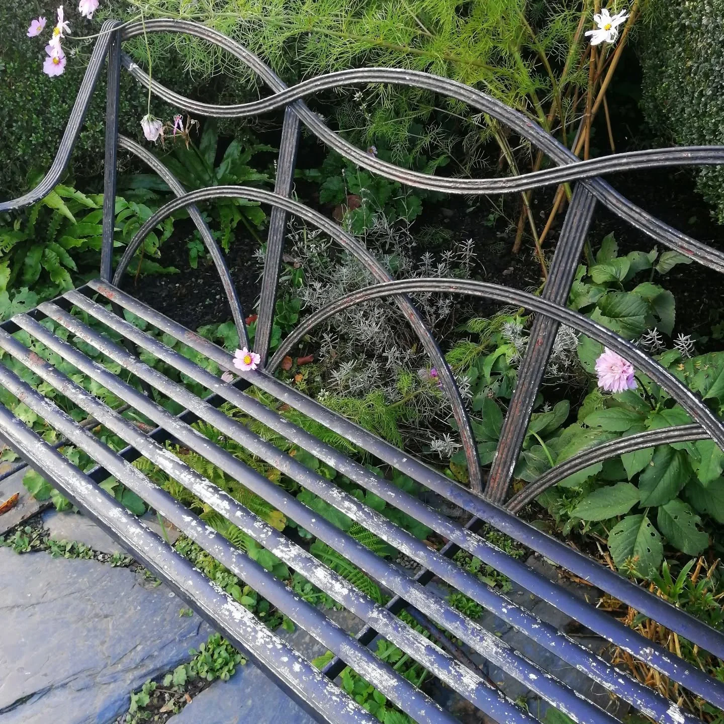 Beautiful ironwork bench in a cottage garden. Reeded details give interest to the back, while curves add a softness appropriate to the garden setting #heritageskills #craft #ironwork #blacksmith #ironbench #metalbench #garden #details #cottagestyle #
