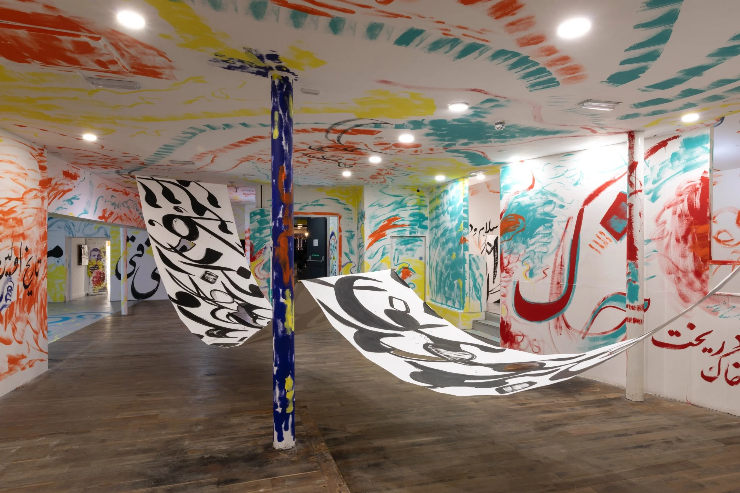 Wide view of the Persian Tour exhibition by Sahar Saki at Elysium Gallery, Swansea, with painted scrolls suspended through the space and vivid Persian calligraphy covering the walls and ceiling.jpeg