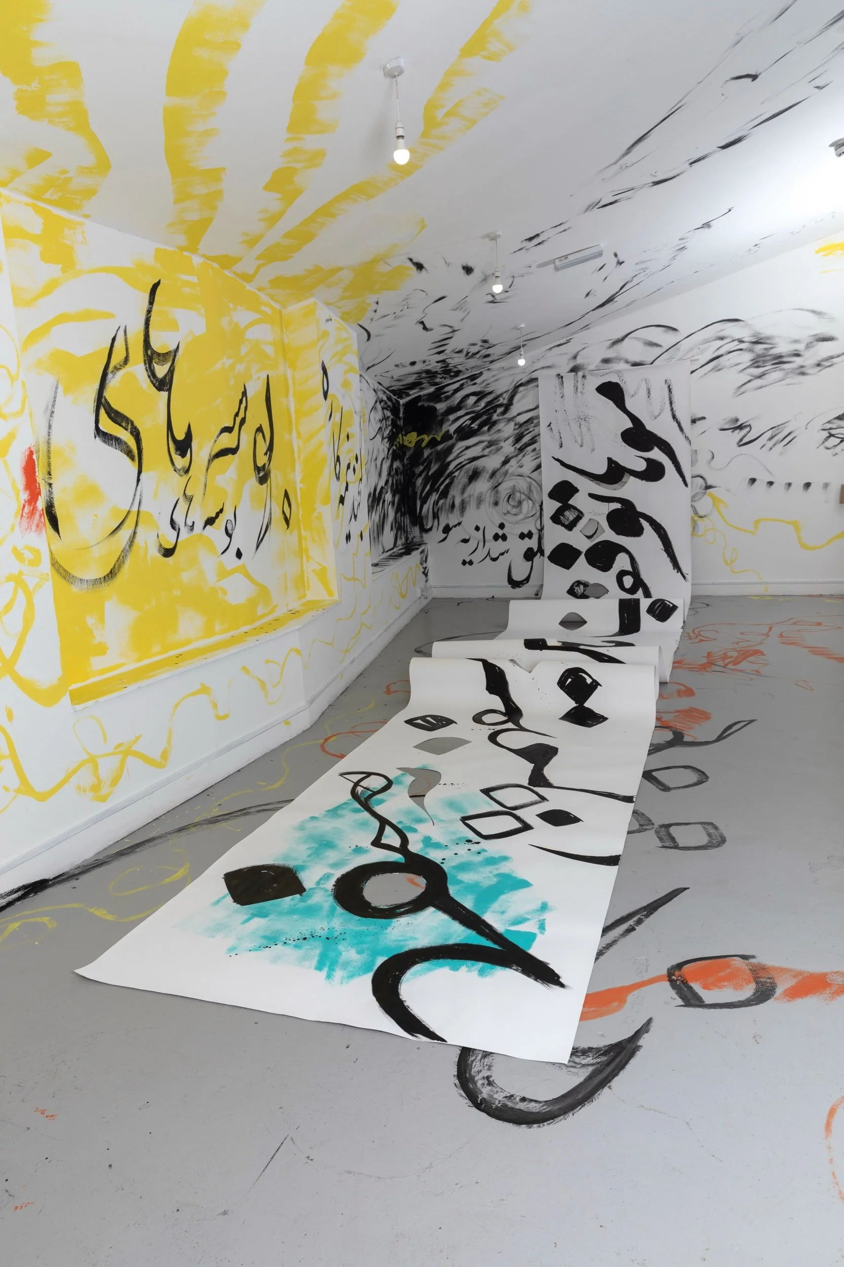 Long view of a suspended scroll in the gallery space, swirling black calligraphy all along it, and on the walls, and very condensed in a far corner.jpeg