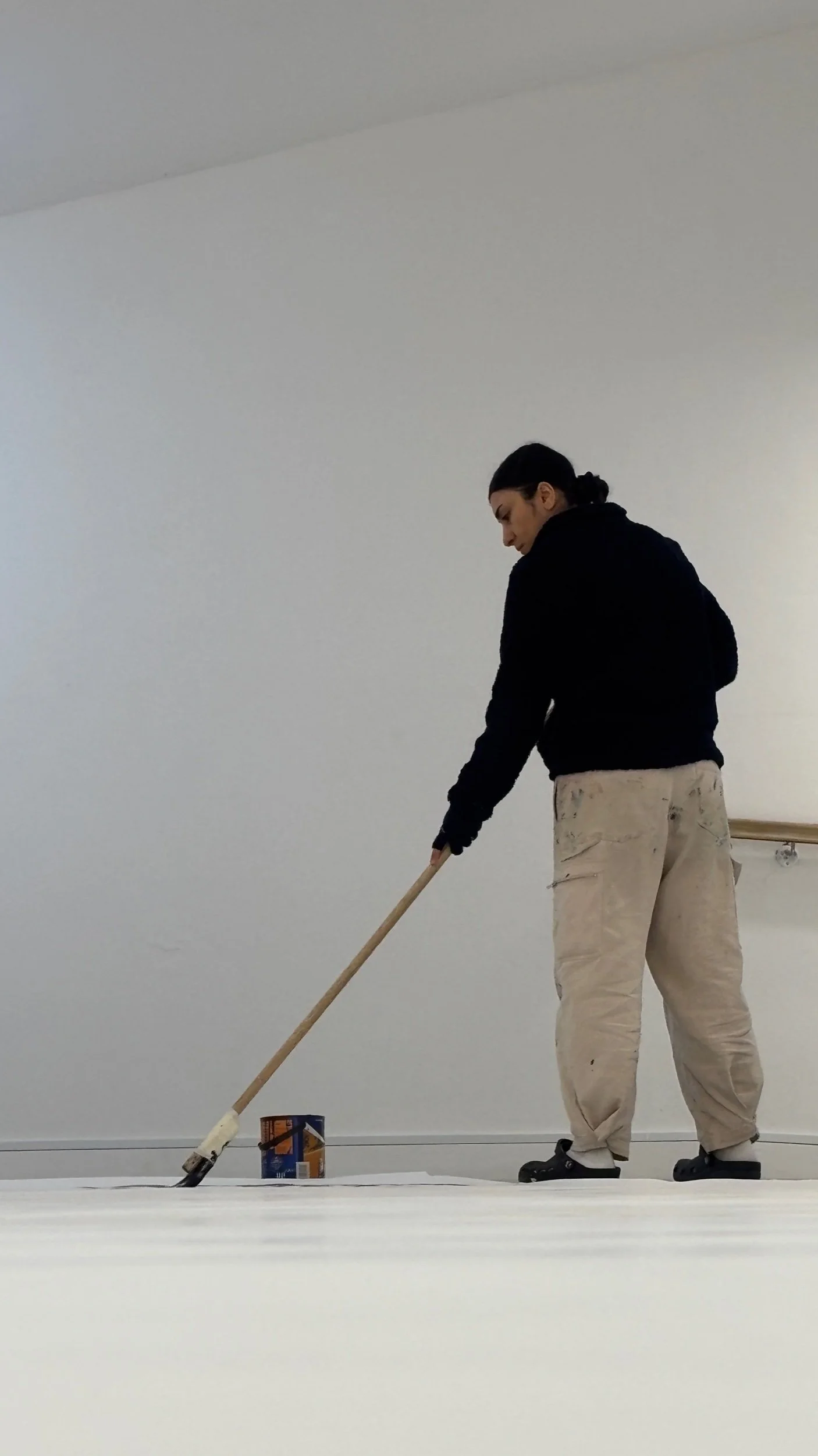 Sahar Saki from the side as she stands with long brush painting the floor in an entirely white space.jpeg