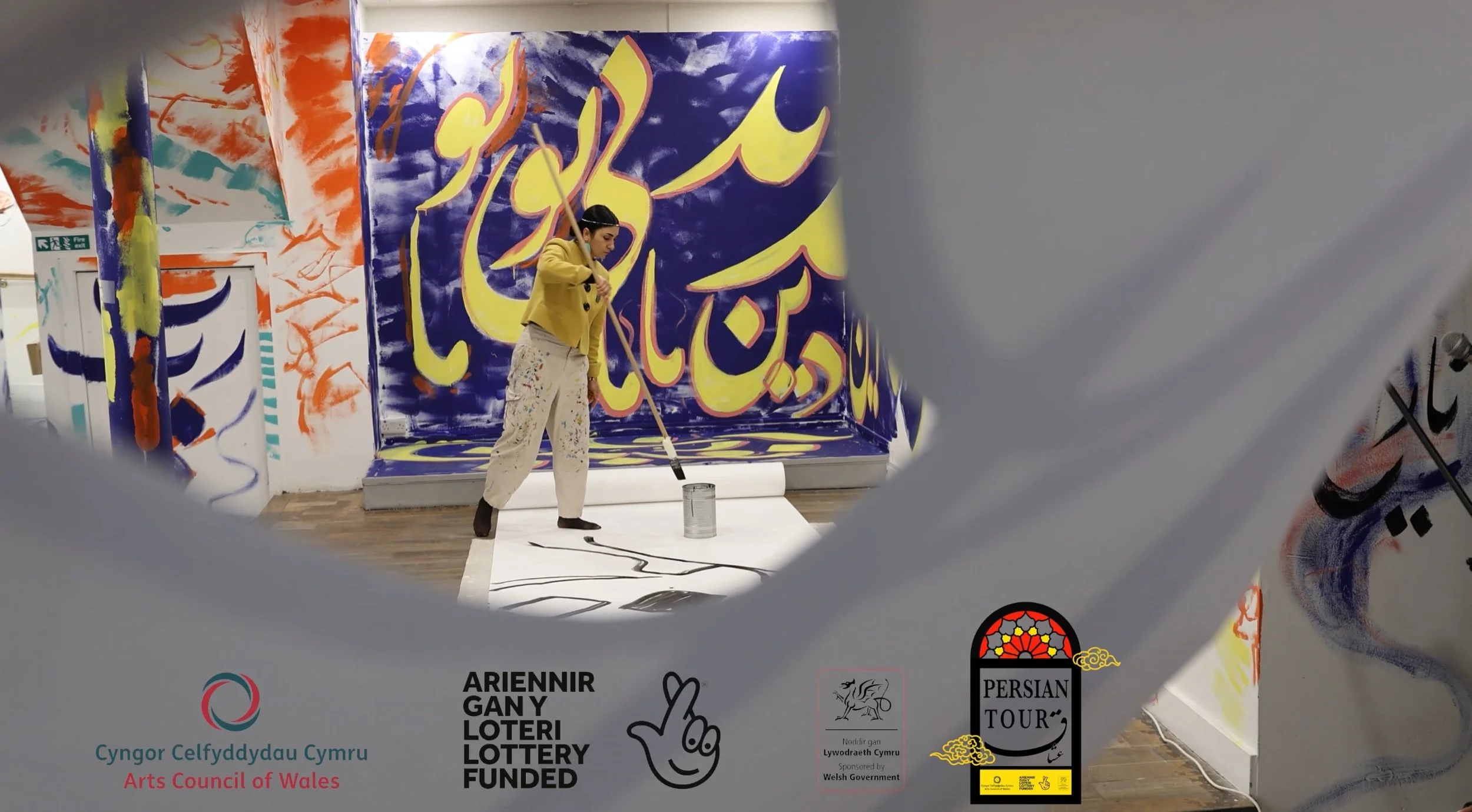 View of Sahar painting a scoll on the gallery floor with a long brush amidst colours immersive calligraphy.jpeg