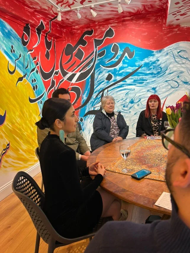 Sahar Saki sat at a table with workshop attendees amidst beautiful colourful calligraphy flowing over the walls and ceiling.jpeg