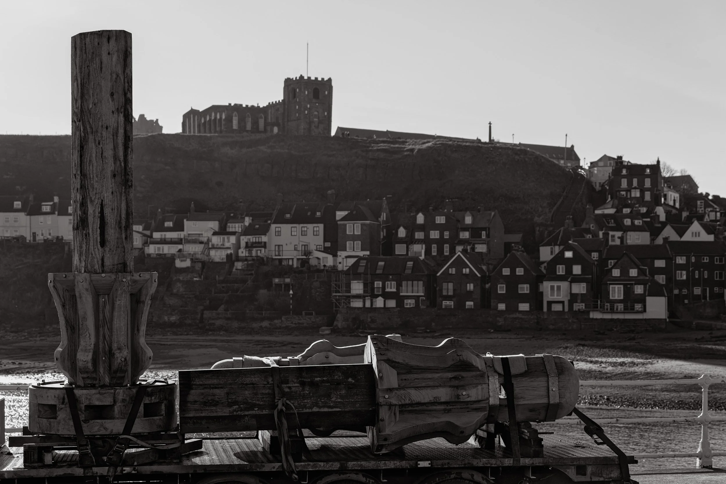 Three completed, hand crafted, timber capstans lie on a trailer with Whitby Abbey and St Mary's church on the Abbey Headland in the background.