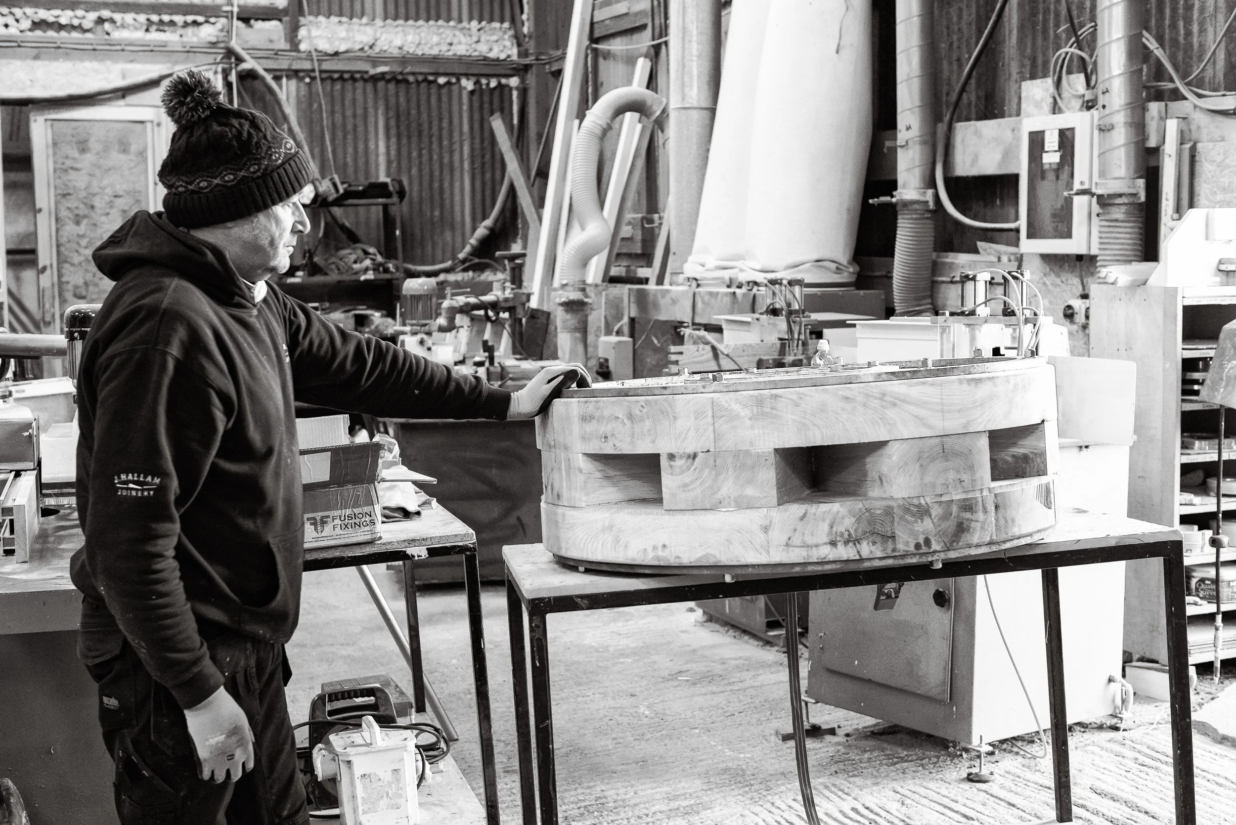 A craftsman rests a hand on a completed component of the replacement capstan created as part of the heritage capstan replacement project at J Hallam Joinery. 