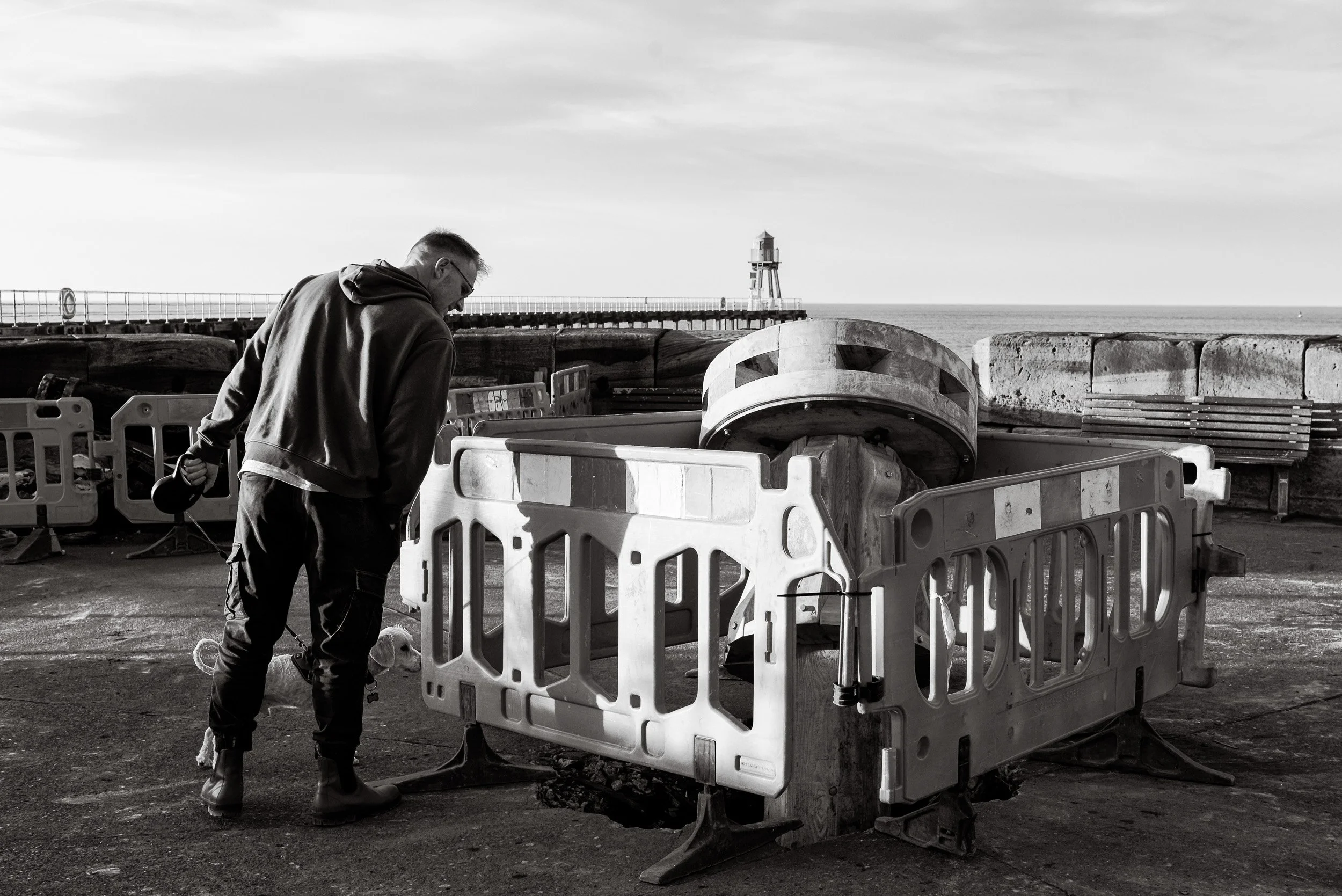 A pedestrian and his dog look with curiosity at the handcrafted timber capstan lying on the pier at Whitby as part of the heritage project to replace the capstans on Whitby Harbour.