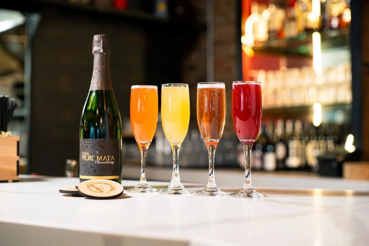Bottle of Cava sparkling wine beside four colorful sparkling wine glasses on a bar counter