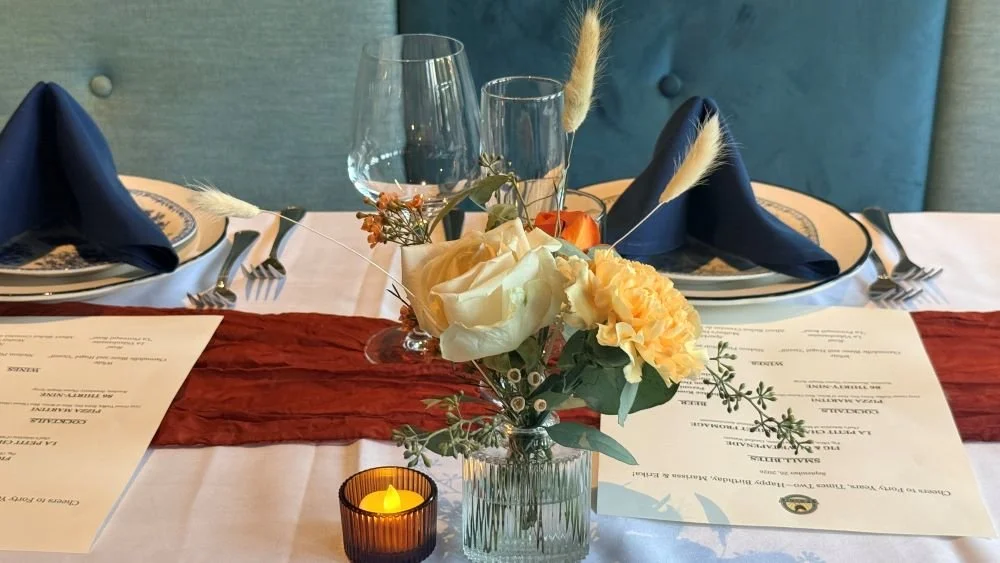 Private dining table set for a party at Le Sud in Roscoe Village, with navy napkins, printed menus, flowers and candlelight