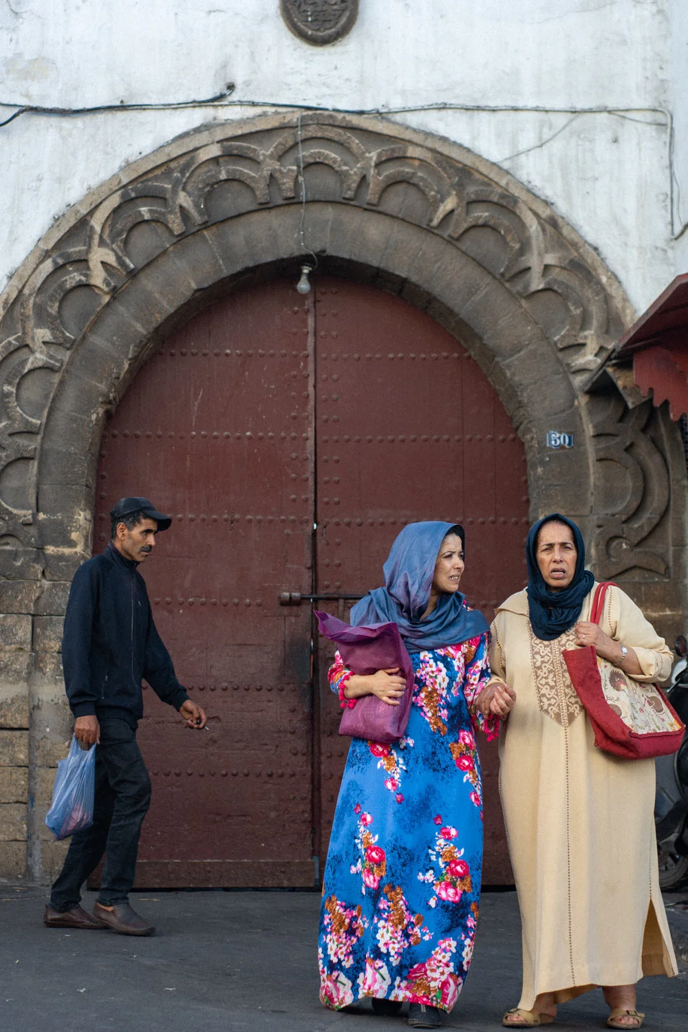 Two women stand outside the wooden doors of the Great Habous Olive Market