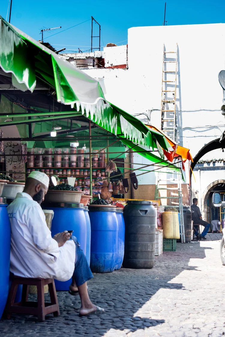 A vendor takes a break to check his phone in front of the ubiquitous blue barrels
