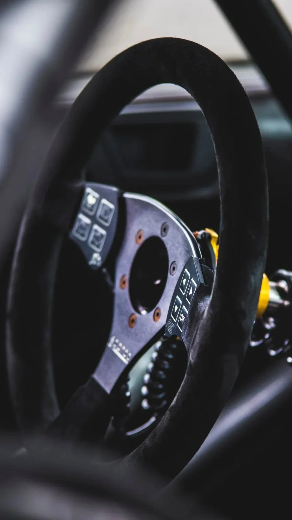Close-up of a racing car steering wheel with buttons, mounted on a racing car interior.