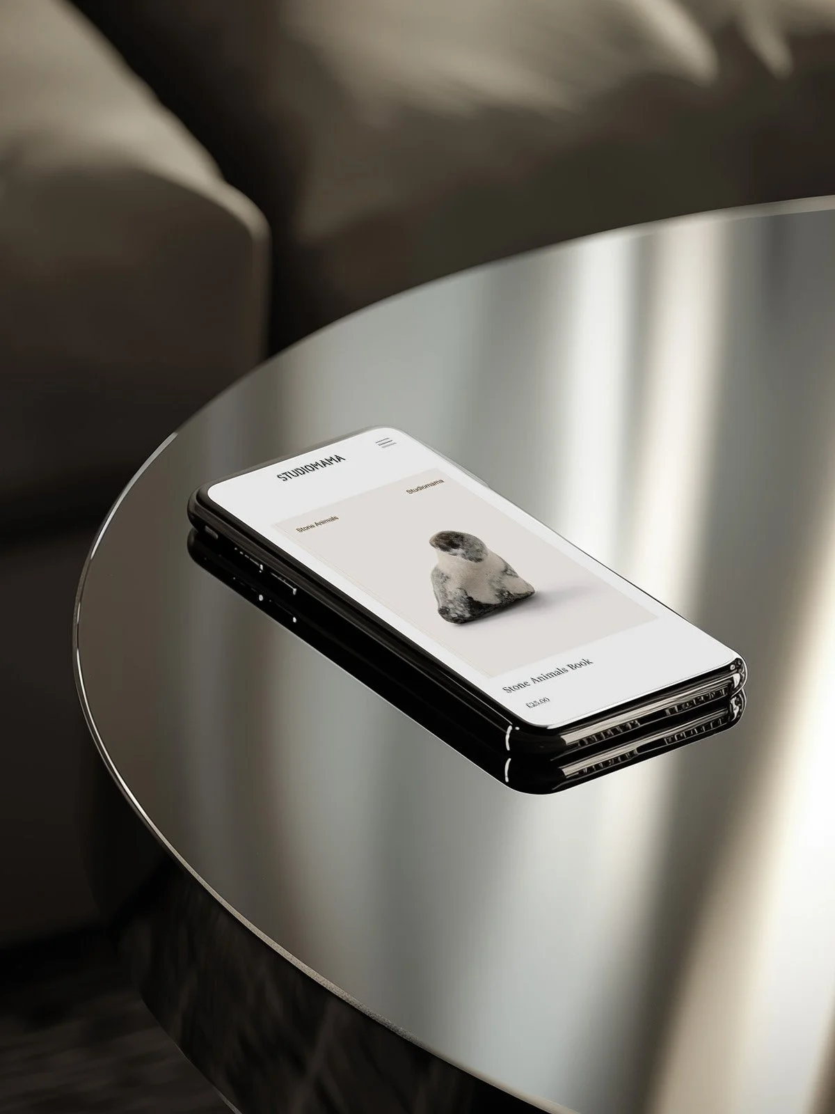 Metallic coffee table with an iPhone showing the Studiomama online store.