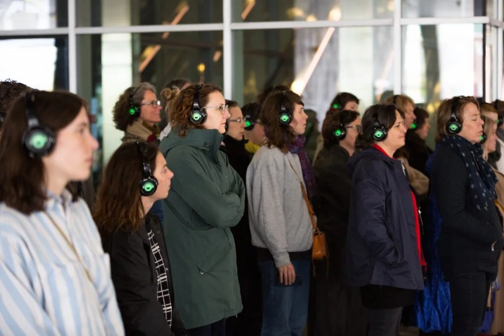 A group of people wearing headphones, many of them have closed eyes.