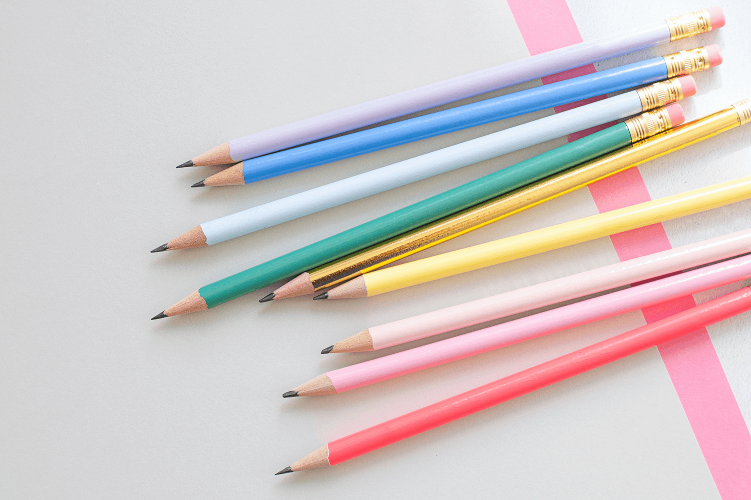 Colorful pencils arranged diagonally on a gray and pink background.