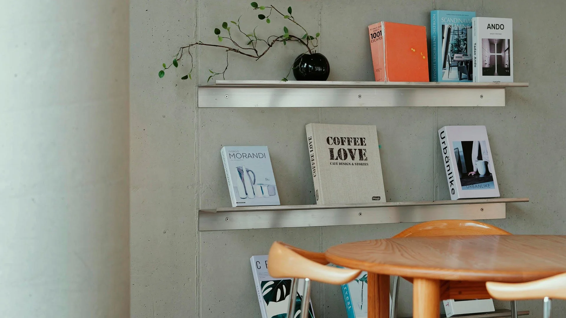 Bookshelf with decorative books, a black vase with a branch and leaves, and a modern wooden chair in foreground.