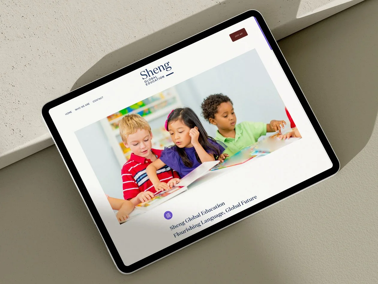 Tablet displaying the homepage of Sheng Global Education website with a photo of children reading together.