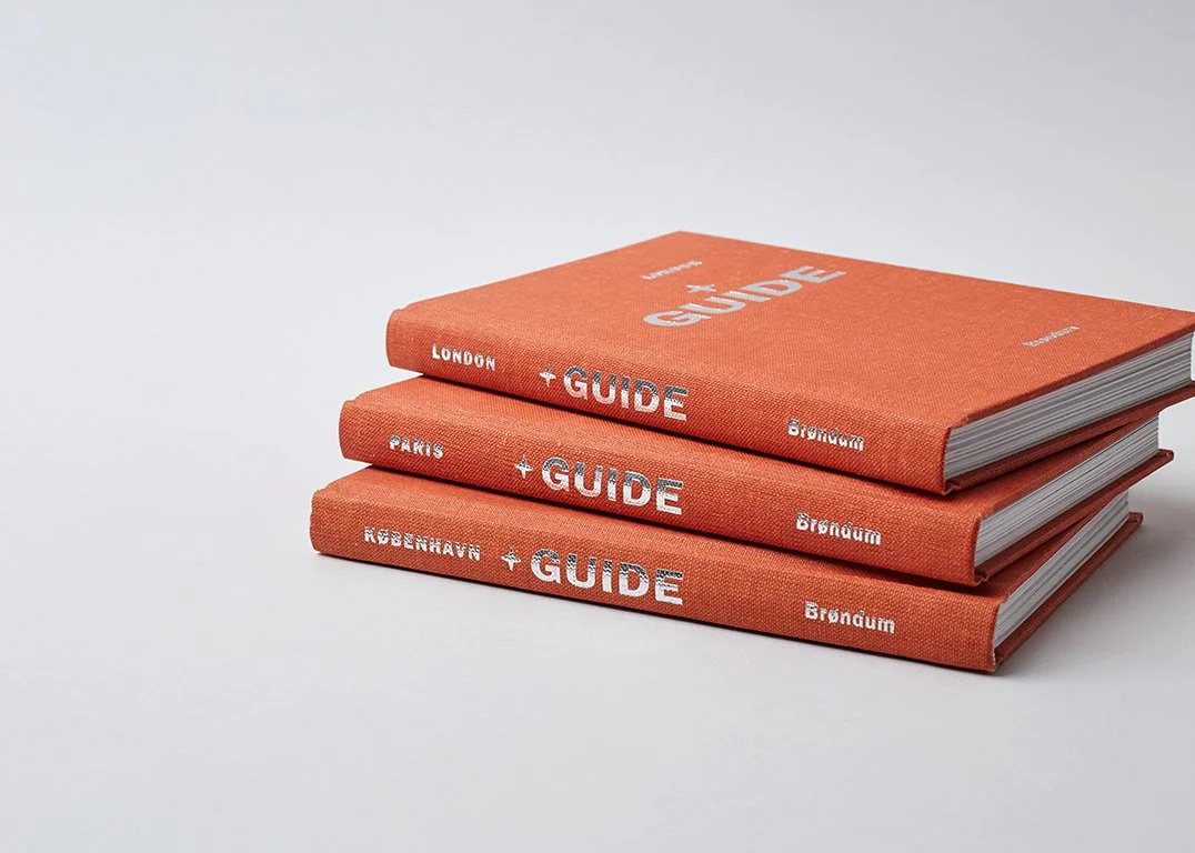 Three orange travel guidebooks stacked, labeled London, Paris, and København.