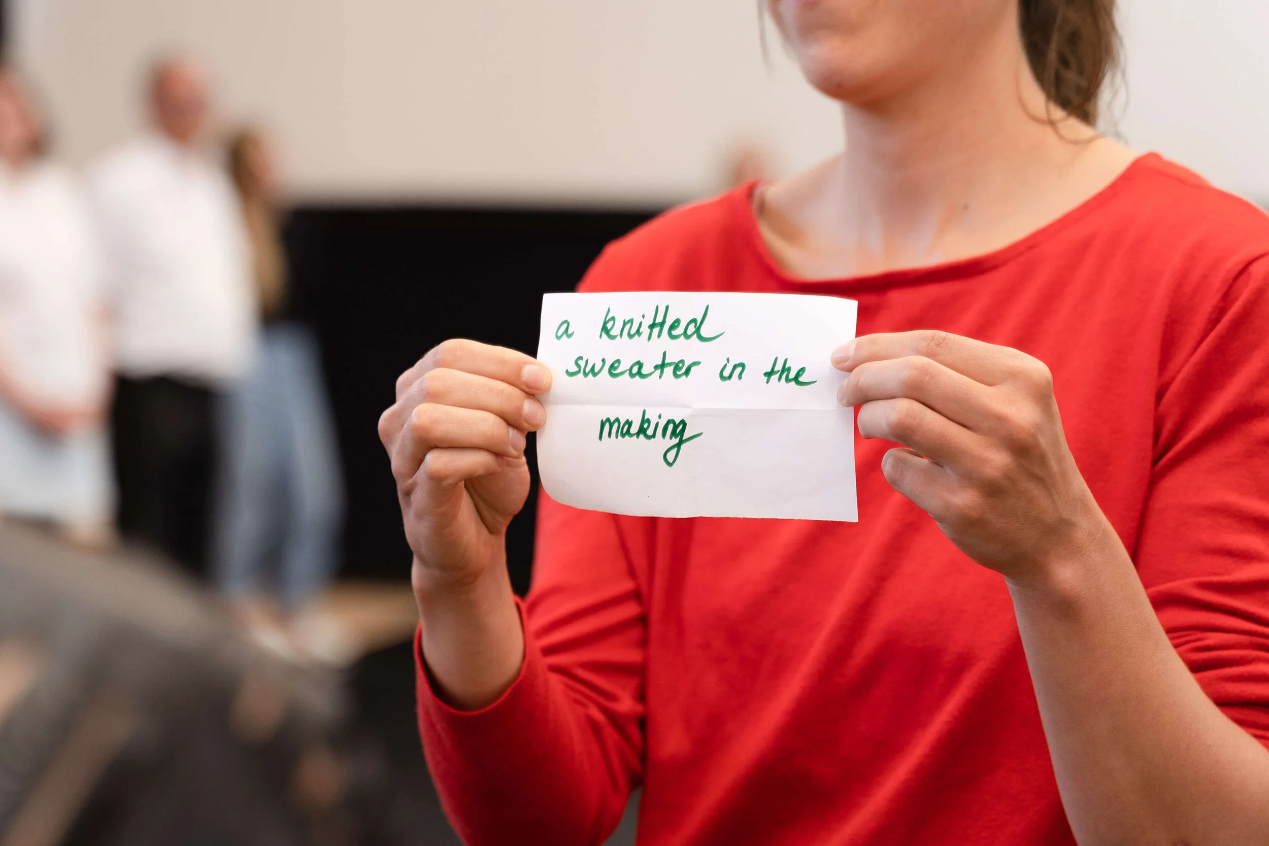 A woman holding up a note with two hands. The note says 'a knitted sweater in the making'.