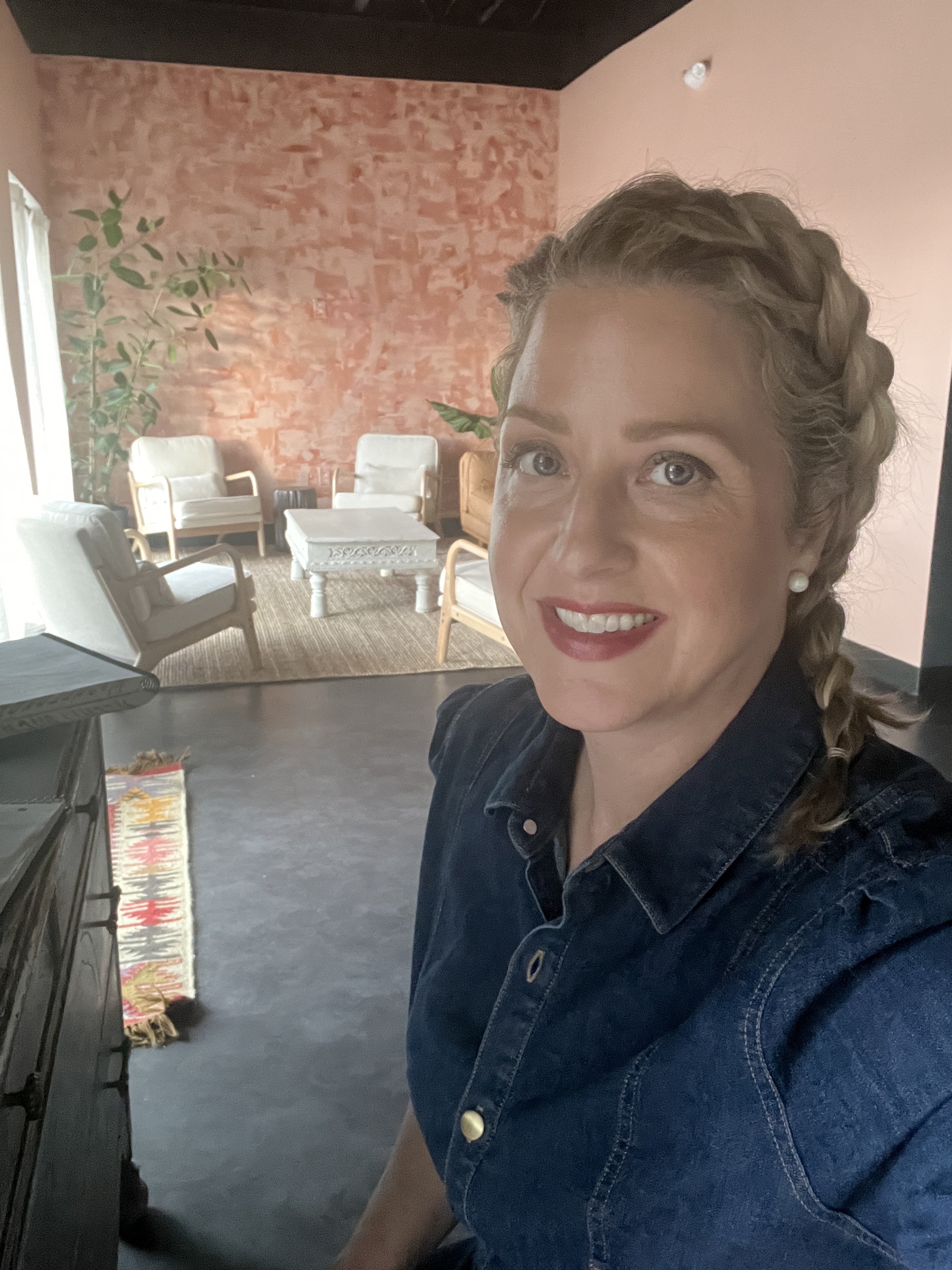 MG sits in her office, wearing a denim shirt, smiling face to camera.