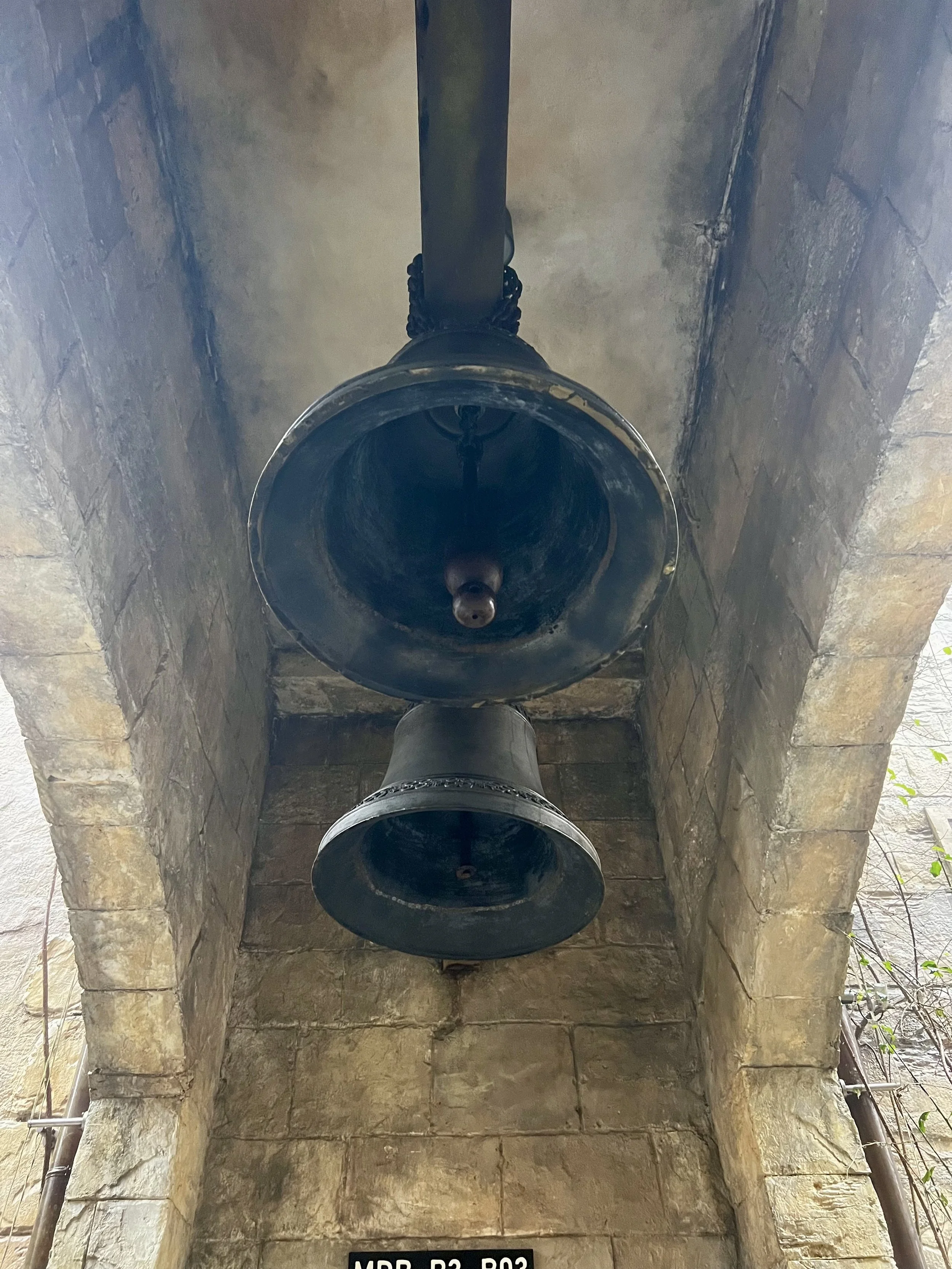 Two large black bells hanging from a stone archway, viewed from below.