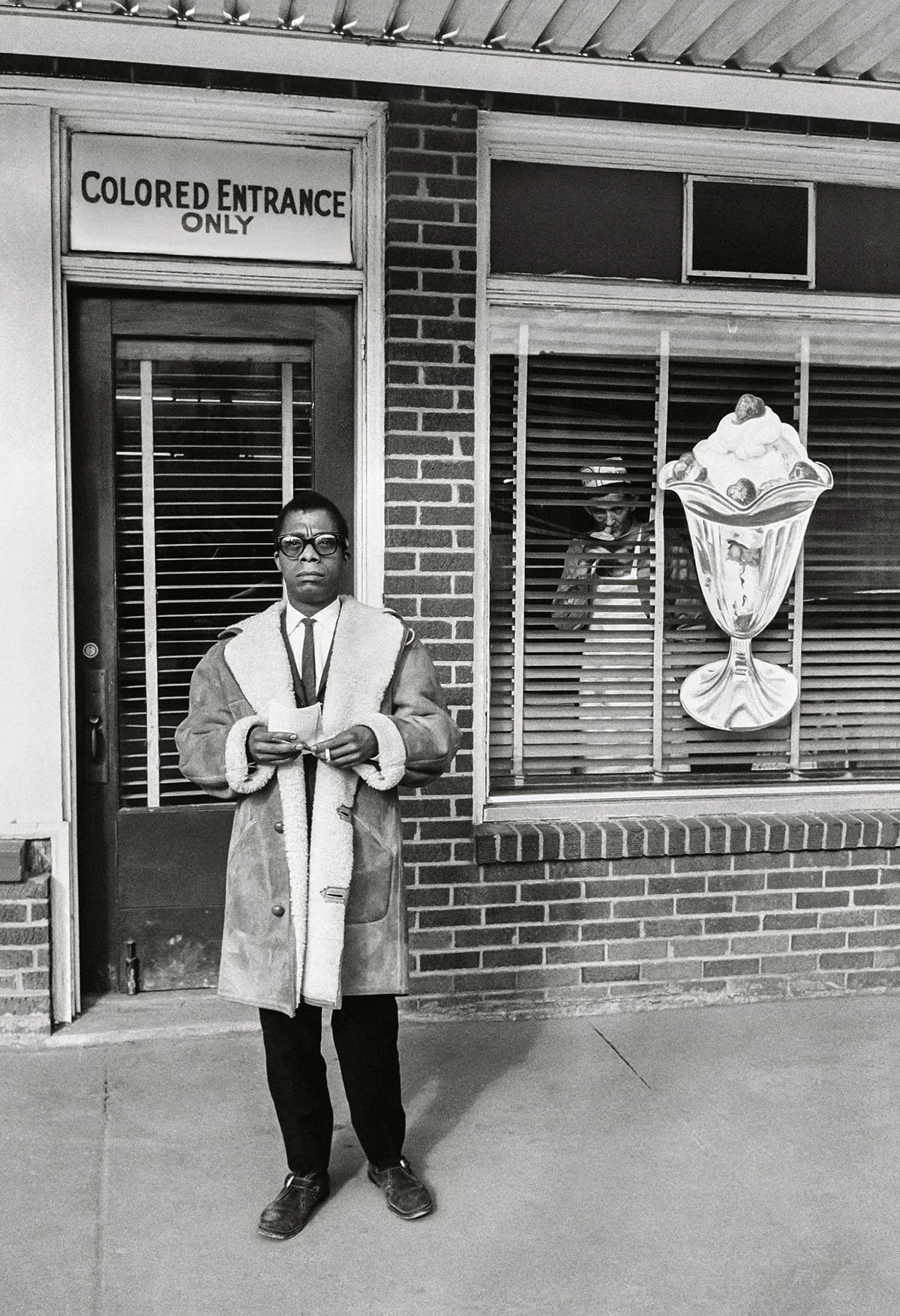 Black and white photo of a person standing outside a building with a sign that says 